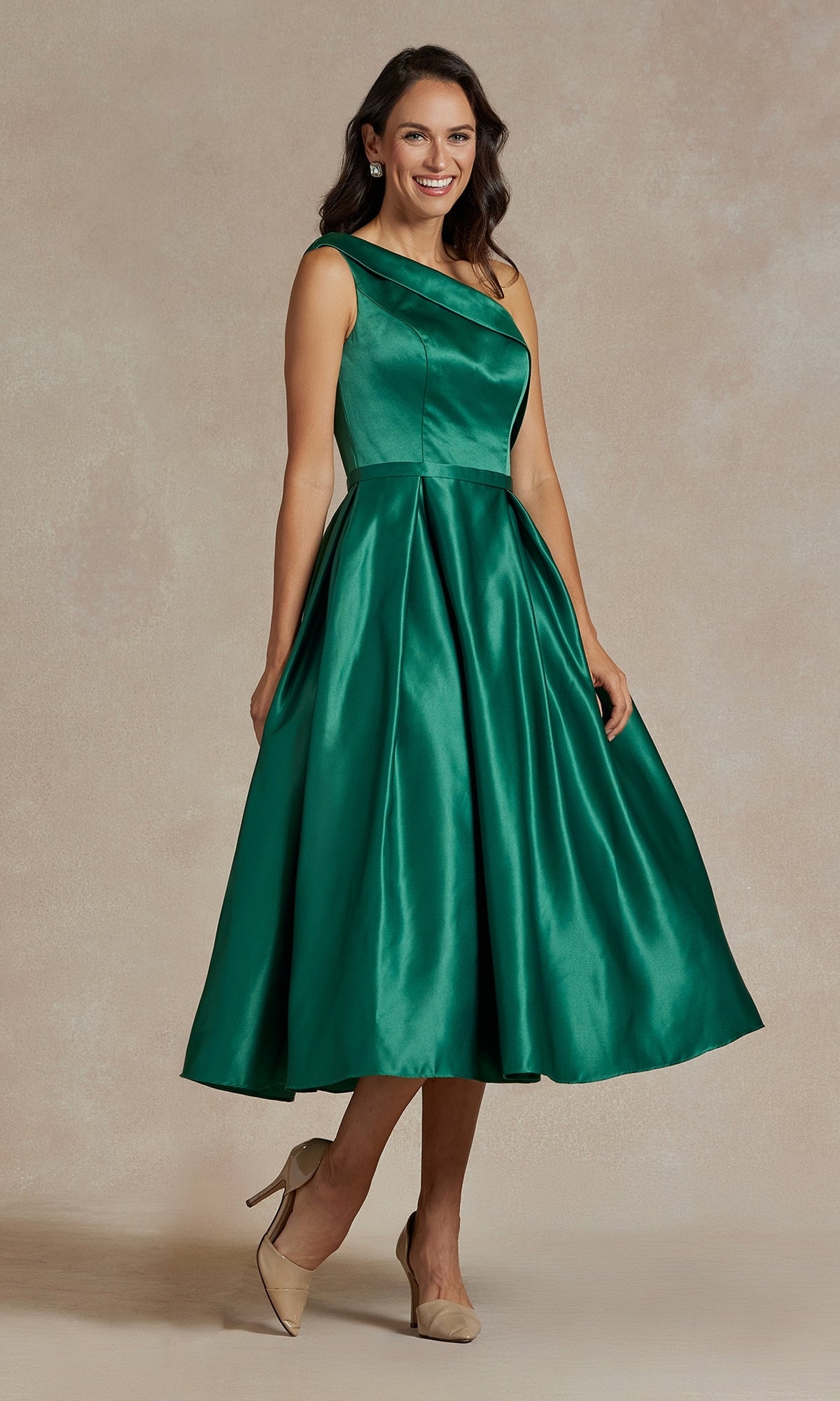 A woman in the One-Shoulder Simple Tea-Length Party Dress JE931, featuring emerald green satin and a flared skirt, pairs it with beige heels and poses elegantly against a neutral background.