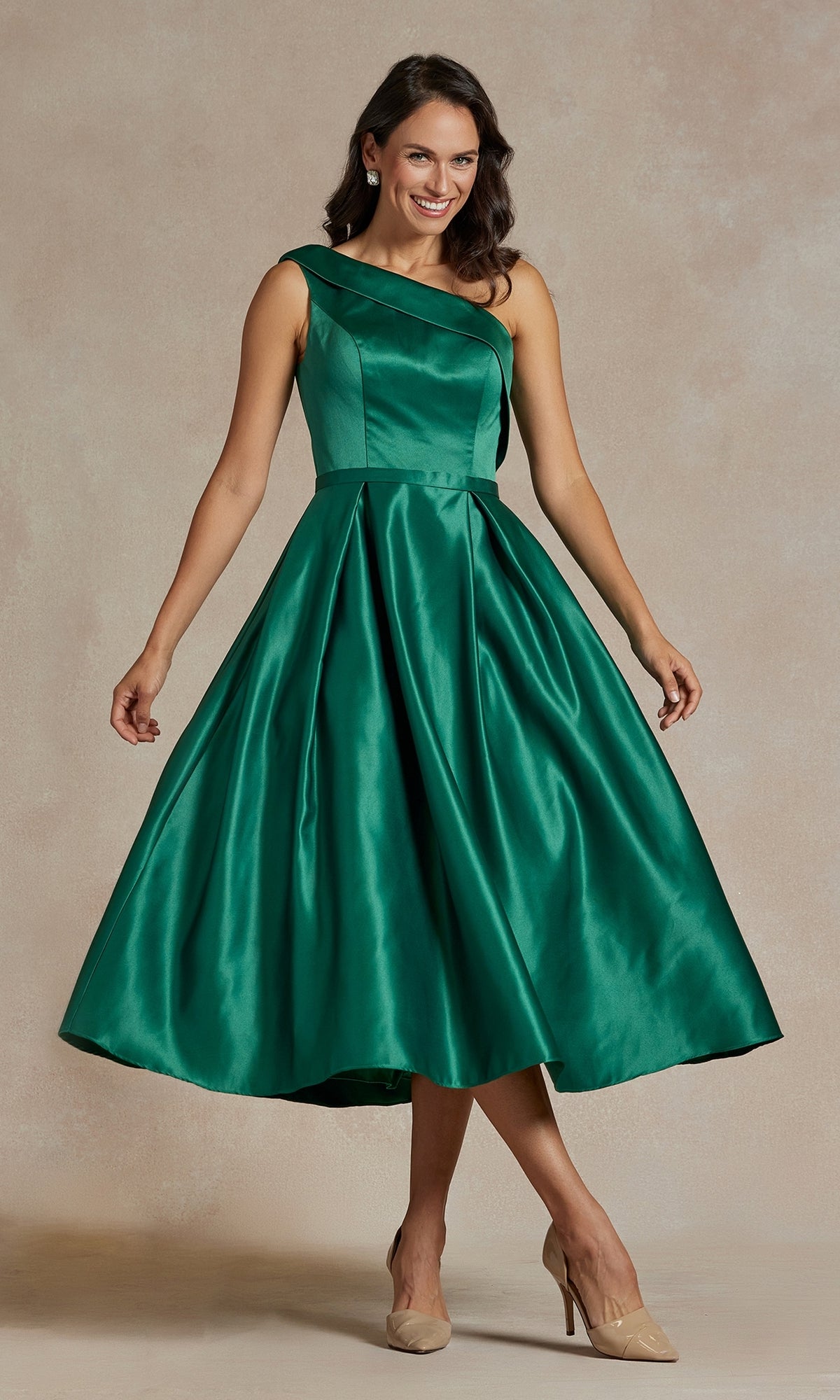 A woman wears the One-Shoulder Simple Tea-Length Party Dress JE931 in emerald green with a flared skirt and beige heels, standing against a neutral background.
