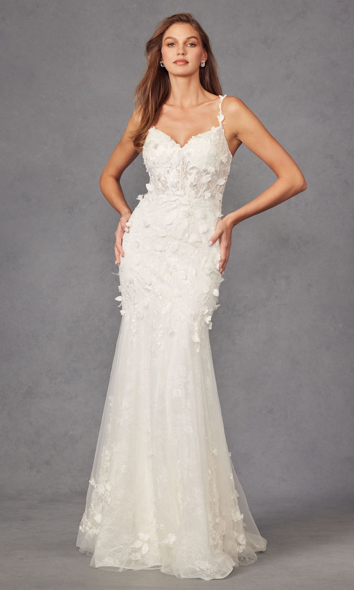A woman wearing the Long Prom Dress JT2475UW by Juliet, an off white mermaid gown with floral appliqué, stands against a gray studio backdrop.