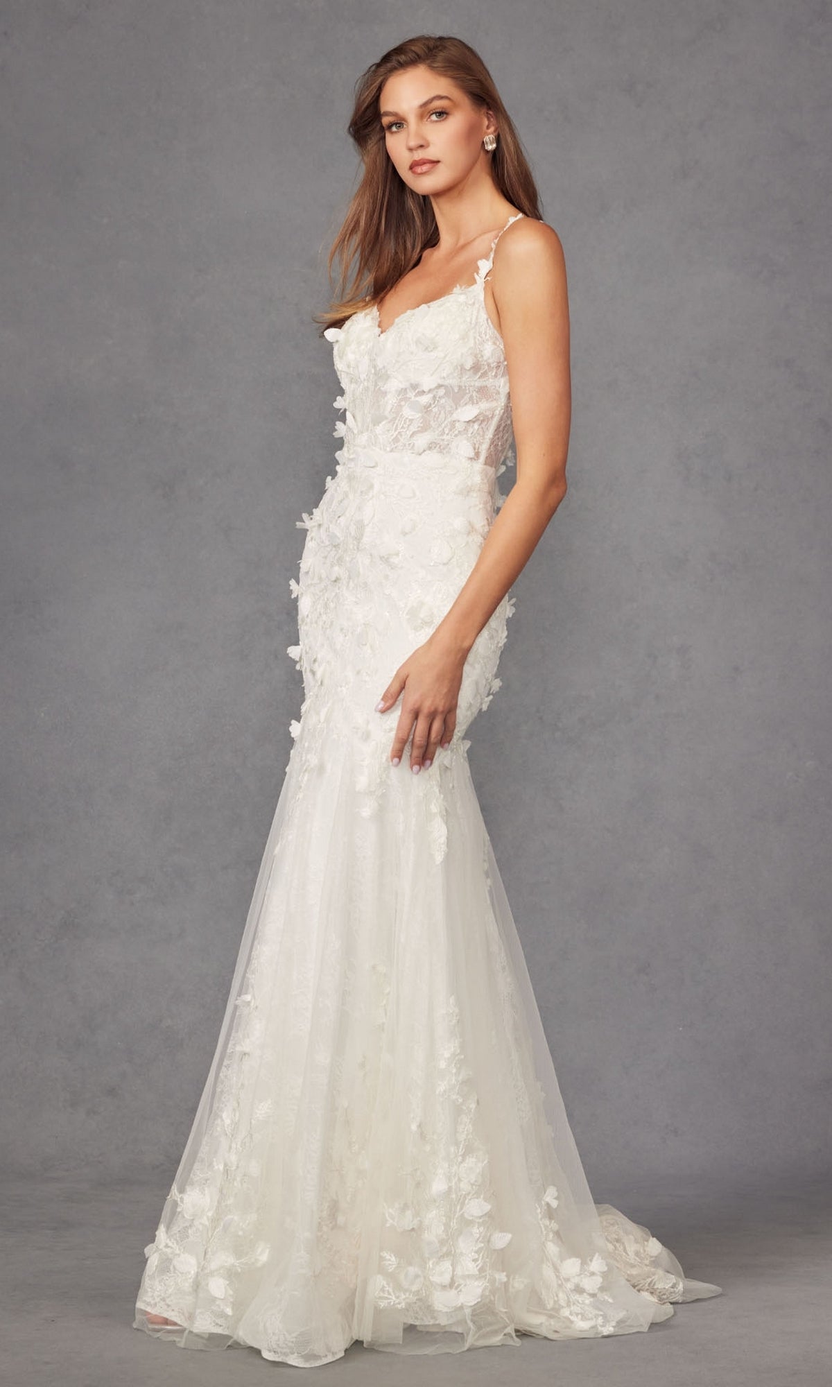 A woman models the Long Prom Dress JT2475UW by Juliet, a fitted off-white mermaid gown with floral appliques, standing against a plain gray background.