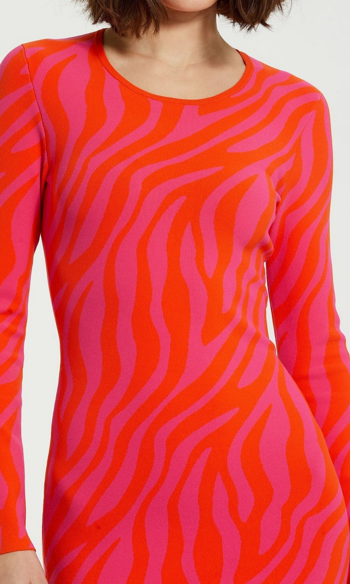 A person wearing the Mac Duggal Pink Casual Wedding-Guest Dress K12008, a long-sleeve pink zebra-print design with bold red and pink stripes. The cropped image shows the upper body and arms, ideal for standout wedding guest inspiration.