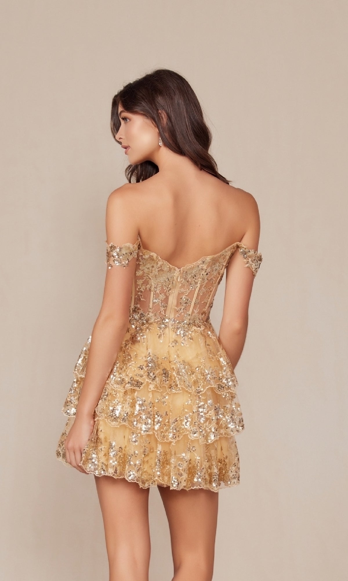 A woman faces away from the camera in the Off-Shoulder Short Ruffled Sequin Hoco Dress K856, featuring gold sequins, a sheer bodice, and a tiered ruffle skirt—perfect for making an entrance at any semi-formal event.