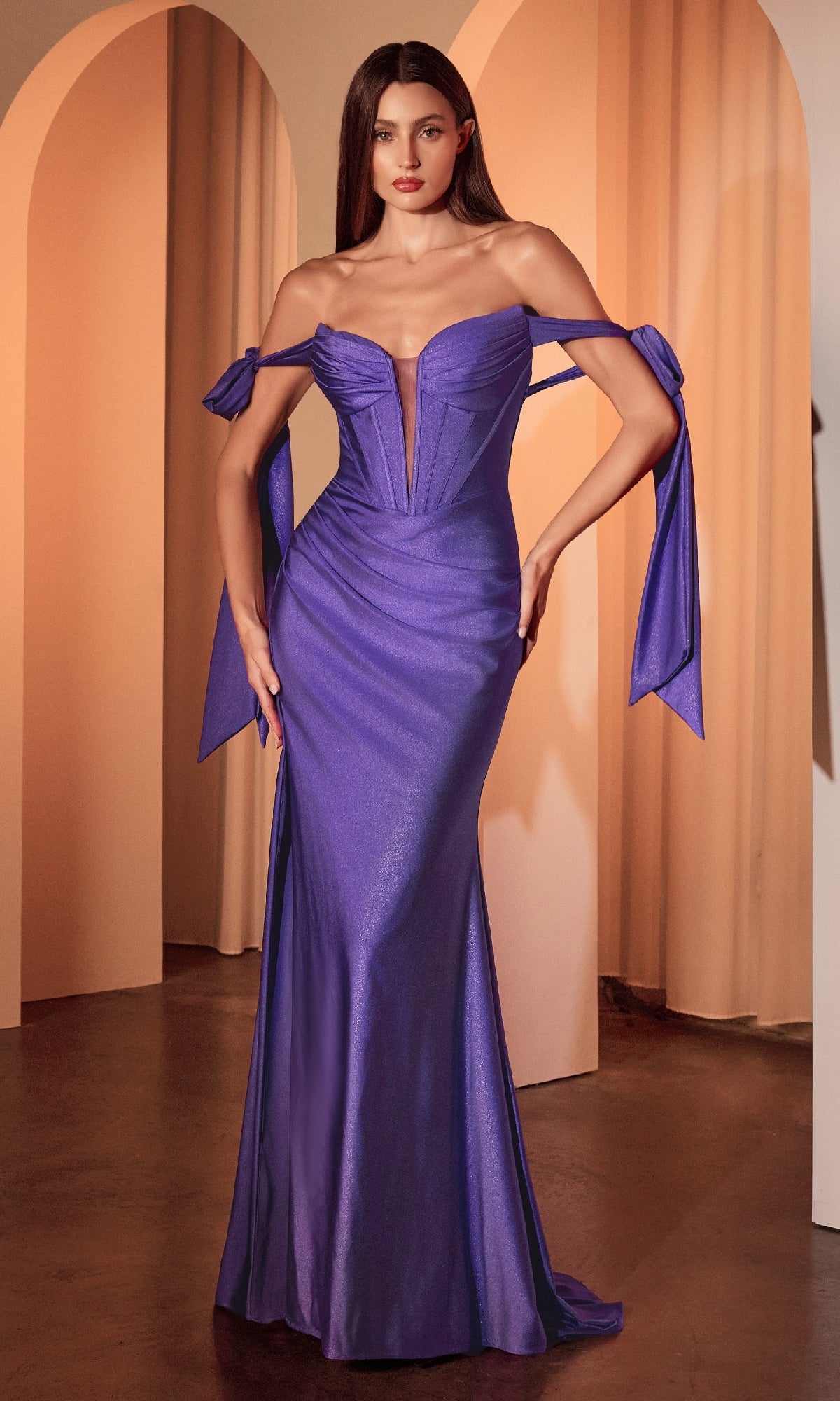 A woman wearing the Shoulder-Bow Long Prom Dress: Ladivine KV1120, featuring tied ribbon sleeves and a corset-style bodice, stands indoors against an arched backdrop.