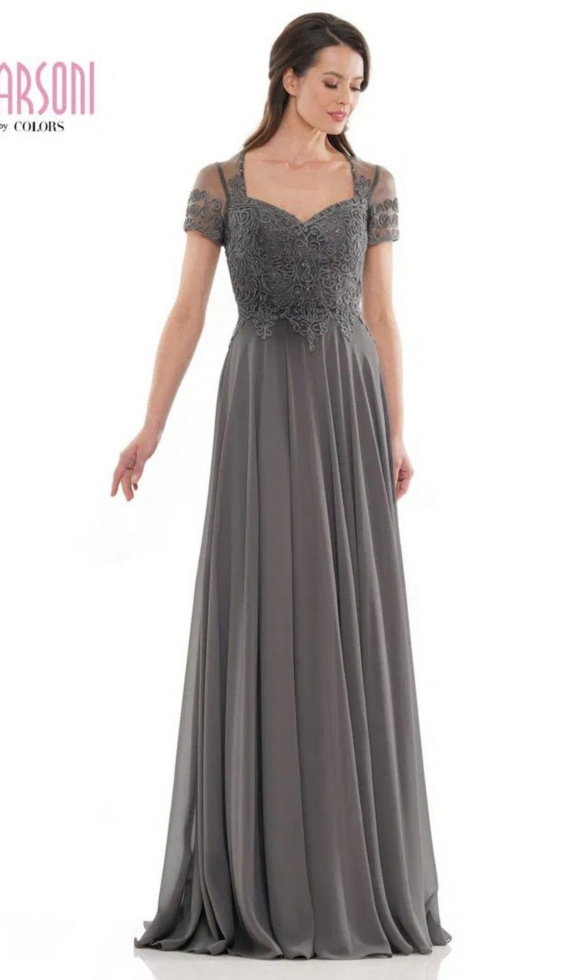 A woman wears the Marsoni M271, a charcoal grey long formal dress with short sleeves, lace bodice details, sheer shoulders, and a pleated chiffon skirt.