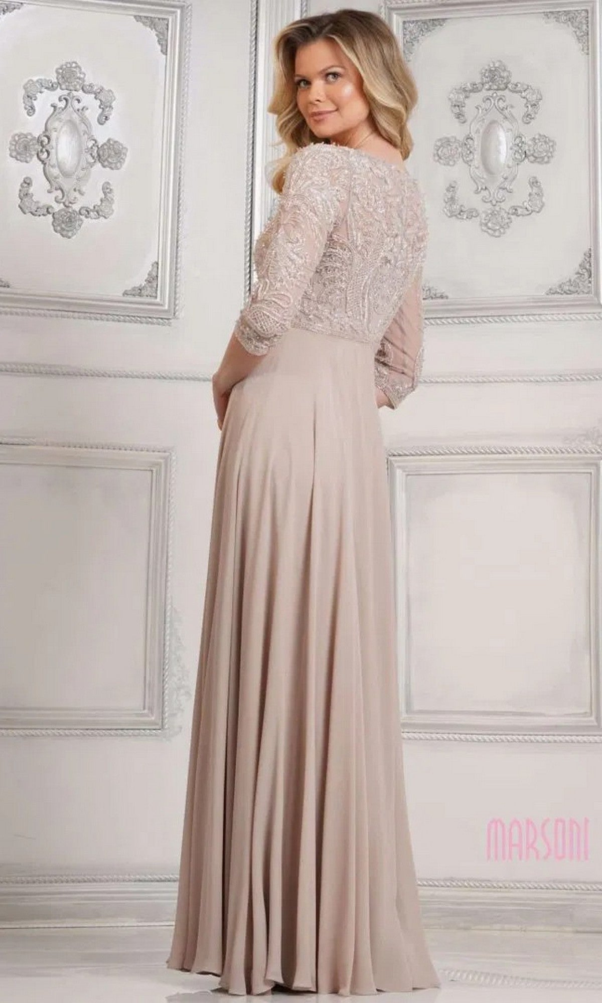 A woman stands in an ornate room wearing the Marsoni MV1322 Long Formal Dress, featuring a modest design with lace embroidered bodice and sleeves.