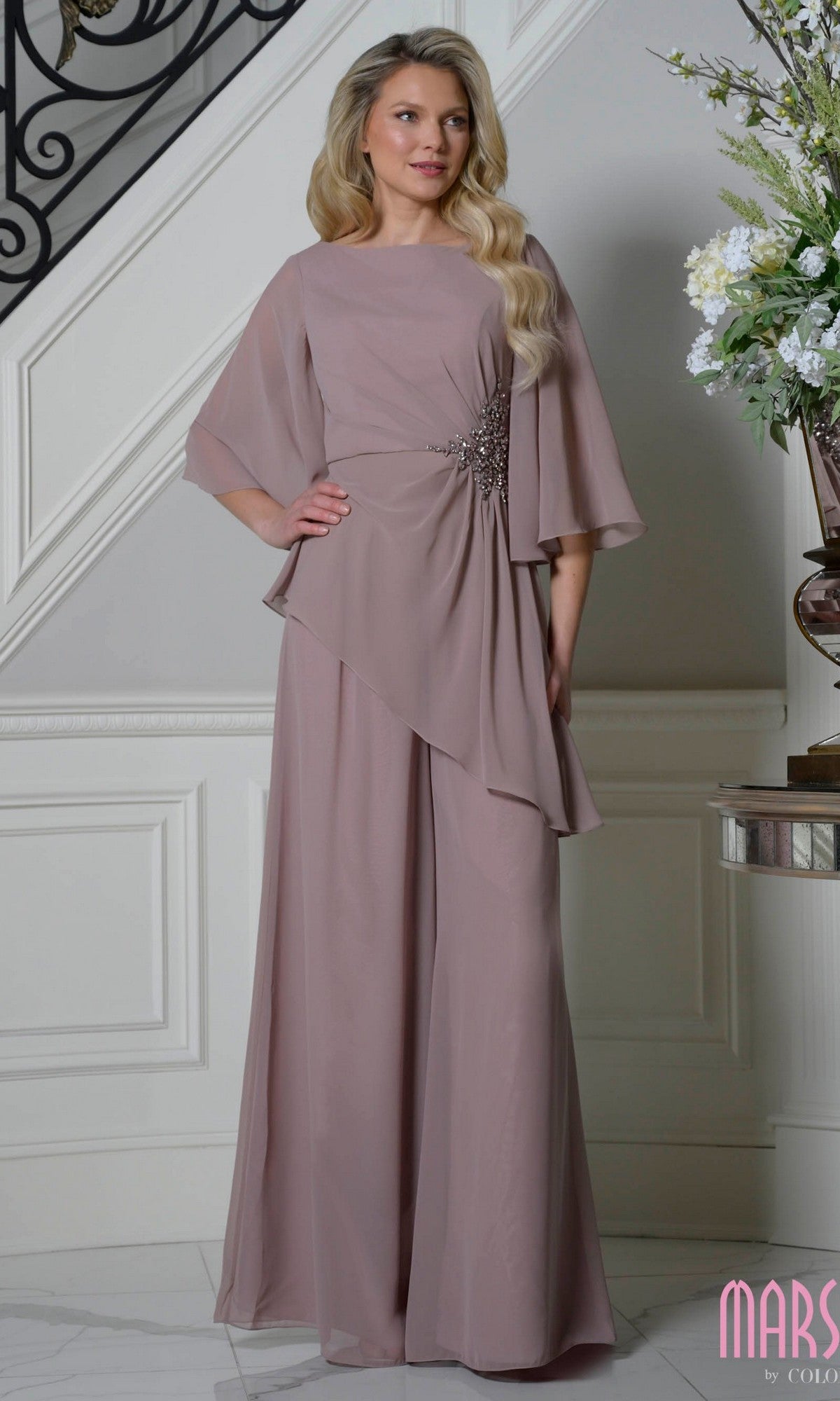 A woman in a mauve Marsoni MV1411 Mother-of-the-Bride pantsuit stands indoors by a staircase.