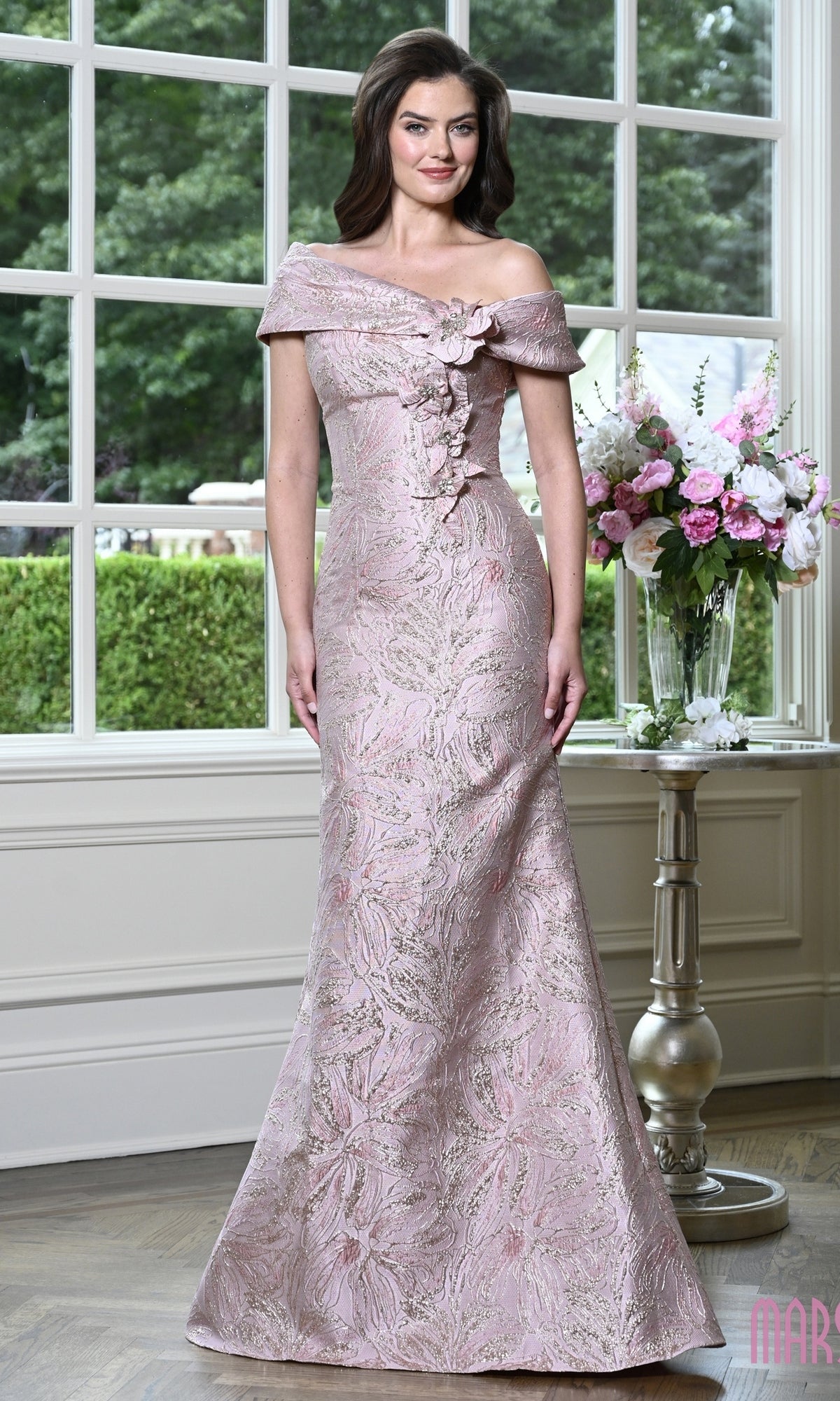 A woman wearing a Long Formal Dress: Marsoni MV1422 in an off-the-shoulder rose floral evening gown with metallic embellishments and an intricate pattern.