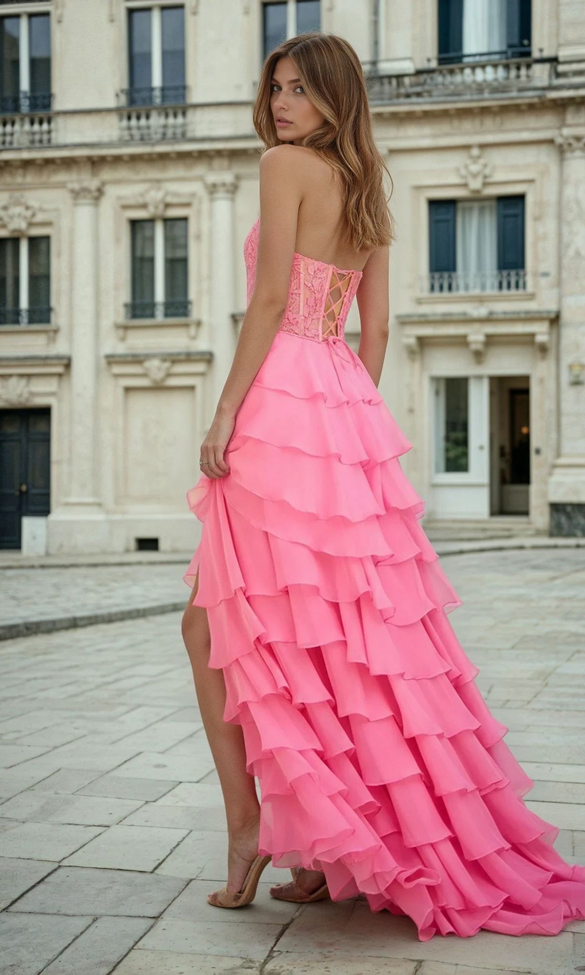 Woman in a pink ruffled floor-length dress standing in front of a classical building.