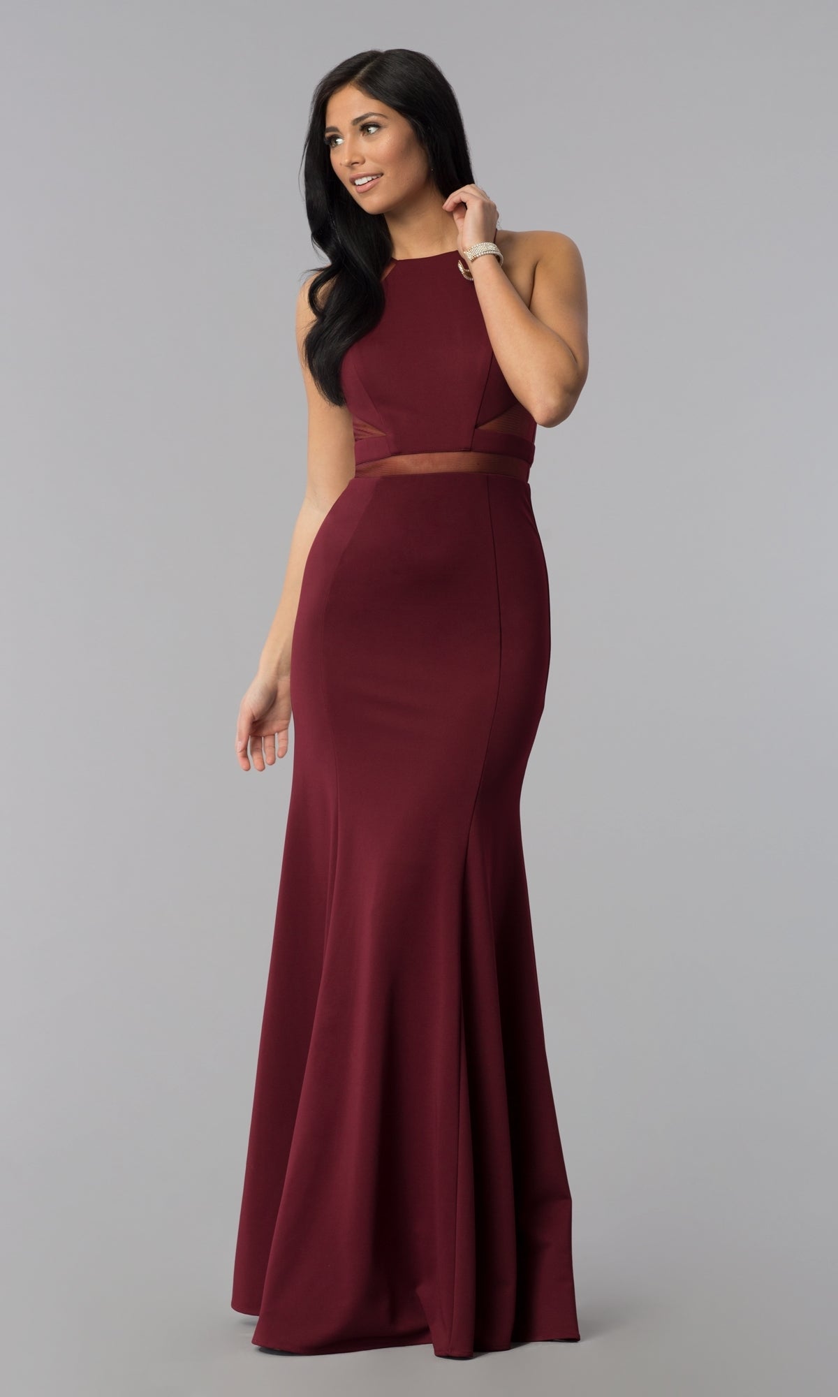 A woman stands against a plain gray background wearing the Illusion-Cut-Out High-Neck Long Prom Dress 8054, a sleeveless, floor-length burgundy gown with a fitted bodice and waist cut-out details.