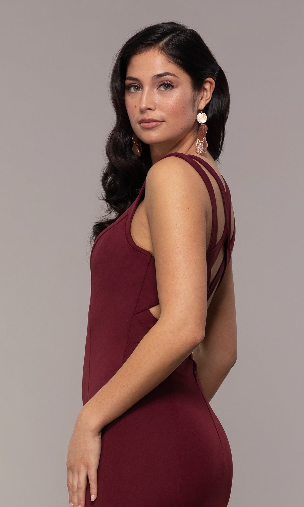 A woman with long dark hair wears the Strappy-Open-Back Long Formal Prom Dress 8232 in burgundy, featuring an elegant open-back and strappy detailing, as she looks at the camera against a neutral background.