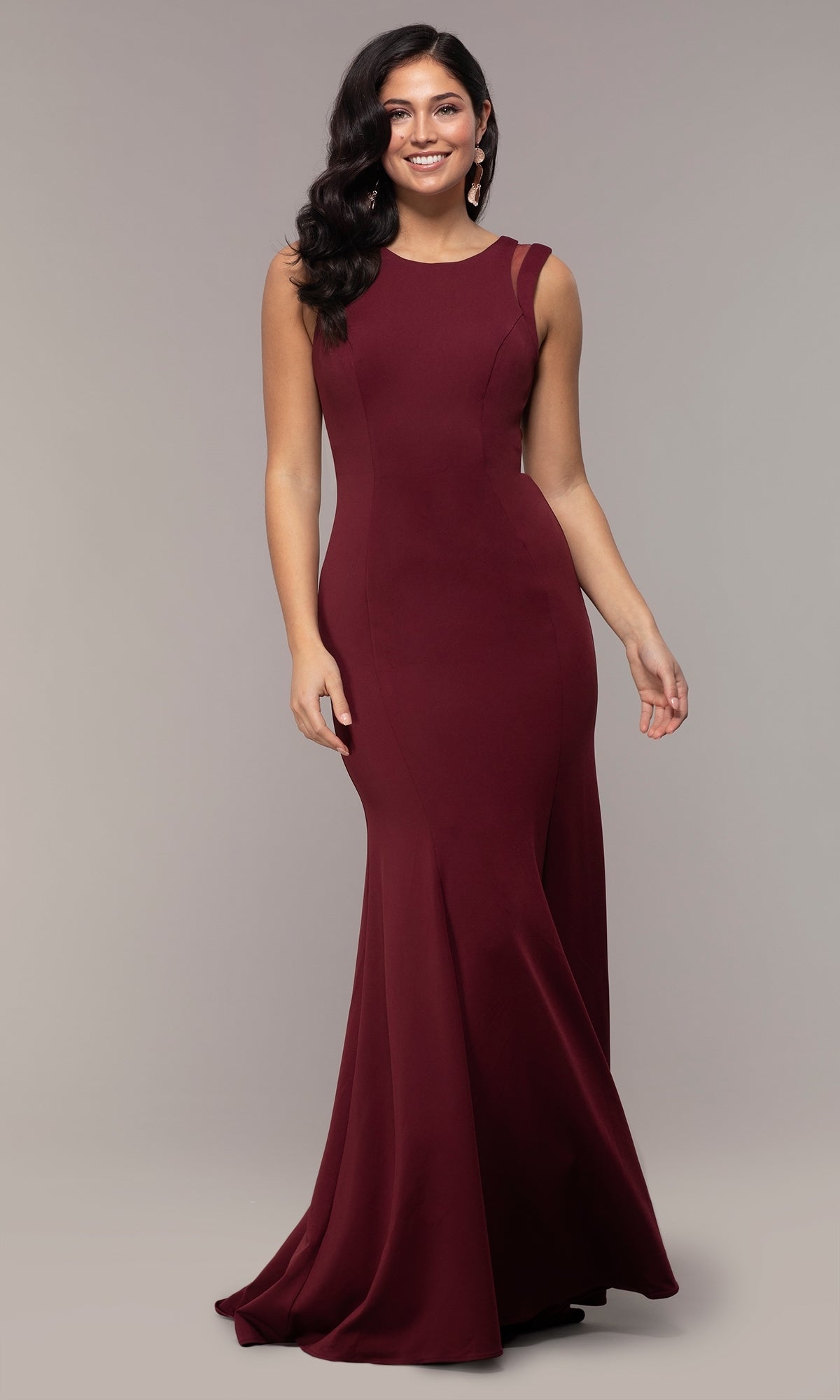 A woman models the Strappy-Open-Back Long Formal Prom Dress 8232, featuring a fitted floor-length burgundy silhouette and open-back straps, standing against a plain gray background.