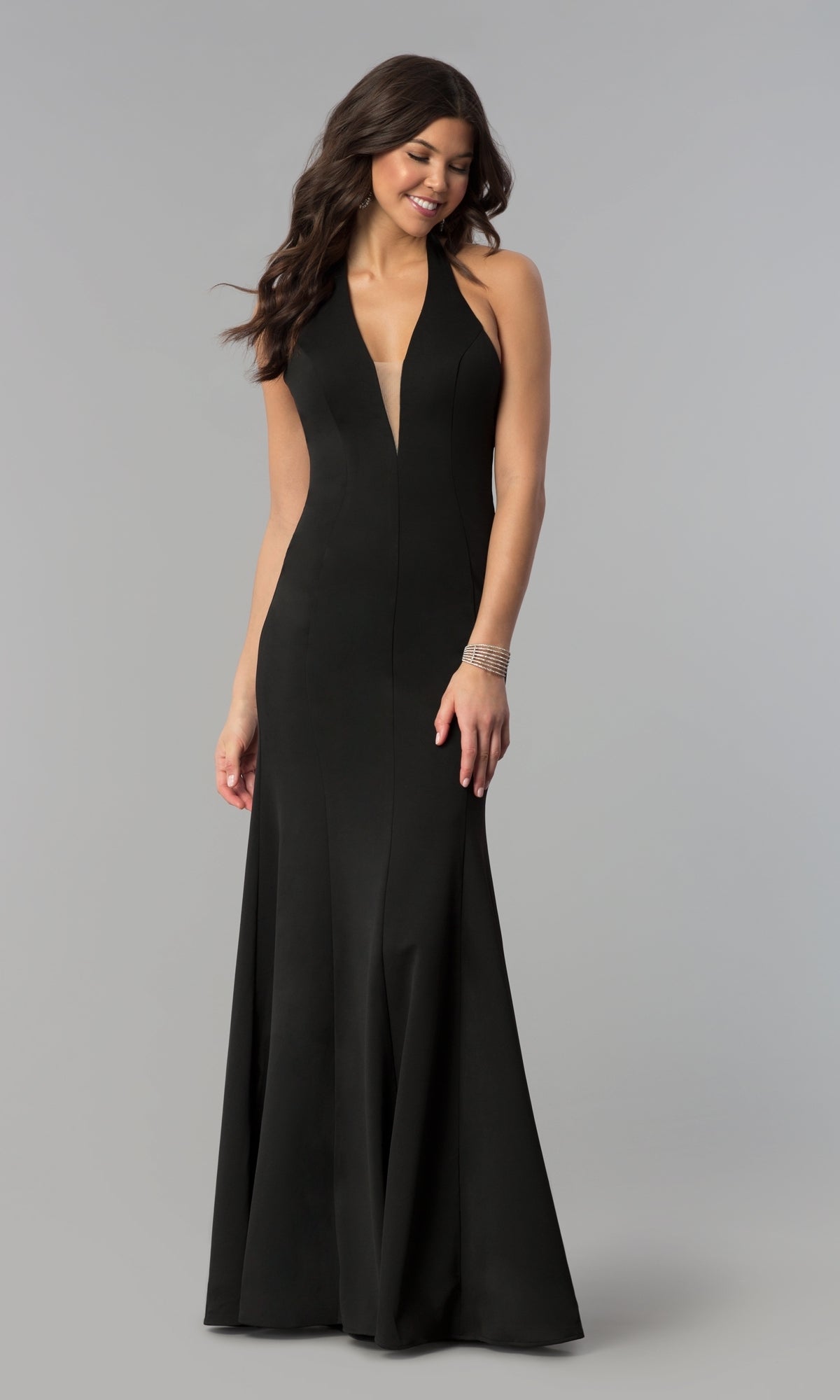A woman wears the Halter V-Neck Long Jersey Formal Prom Dress 8262 in black, a sleeveless, floor-length gown with a deep V-neckline, standing against a plain gray background.