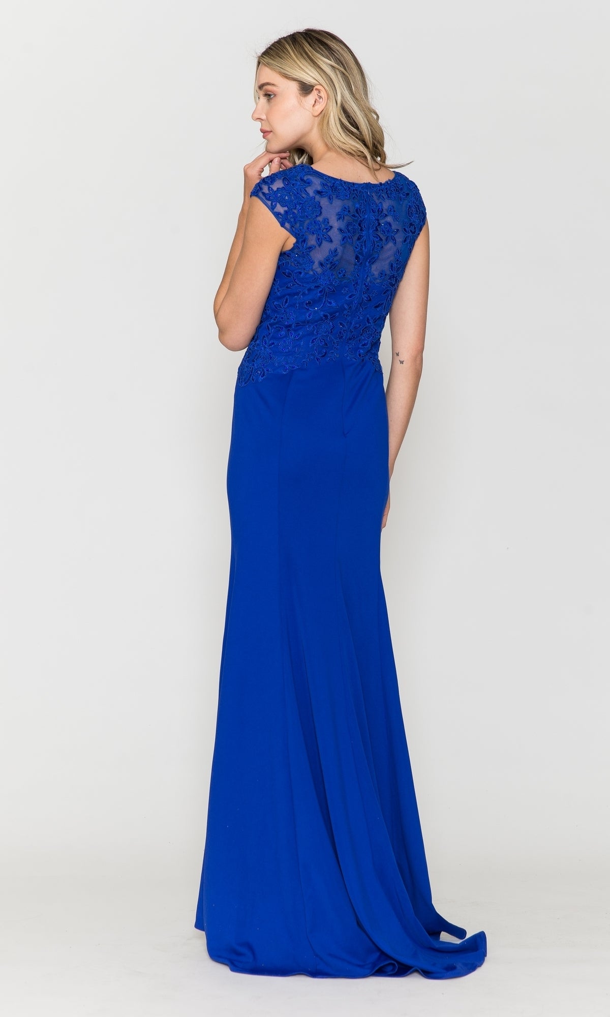 A woman stands facing away, wearing the Cap-Sleeve Embroidered Jersey Long Prom Dress 8558 in royal blue, featuring a floor-length skirt, cap sleeves, and an elegant lace bodice.