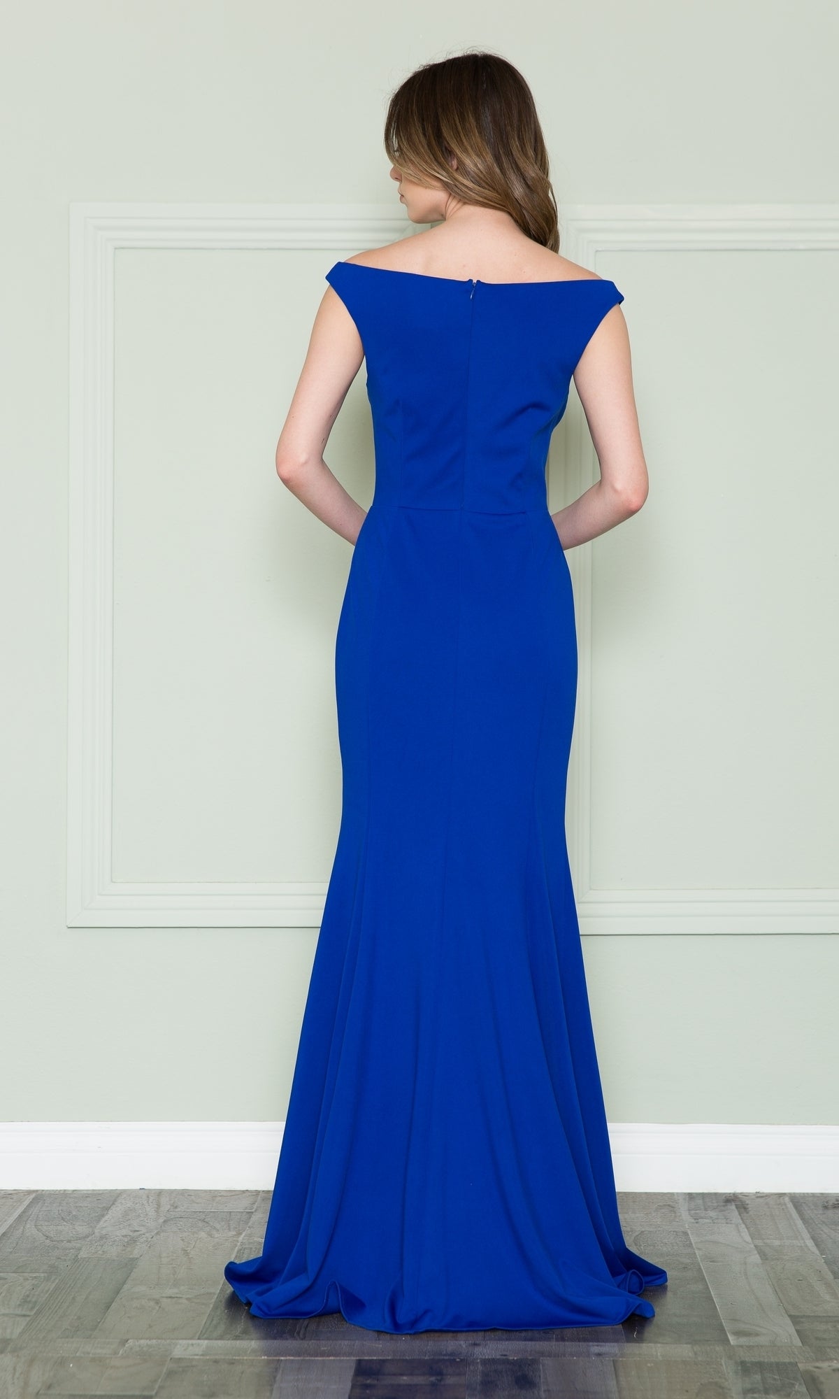 A woman wearing the Off-the-Shoulder Classic Long Prom Dress 8724 in royal blue stands with her back to the camera, facing a pale green wall.