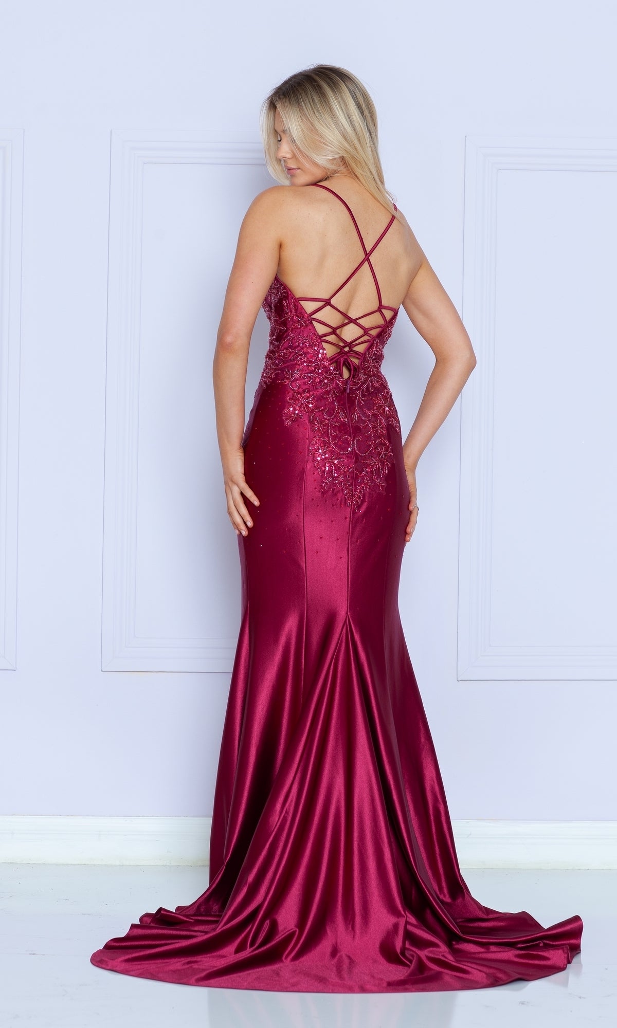 A woman poses against a light wall in the Embroidered-Lace-Bodice Long Jersey Prom Dress 9142—a stunning floor-length formal gown with embroidered lace bodice and crisscross open back, all for under $250.