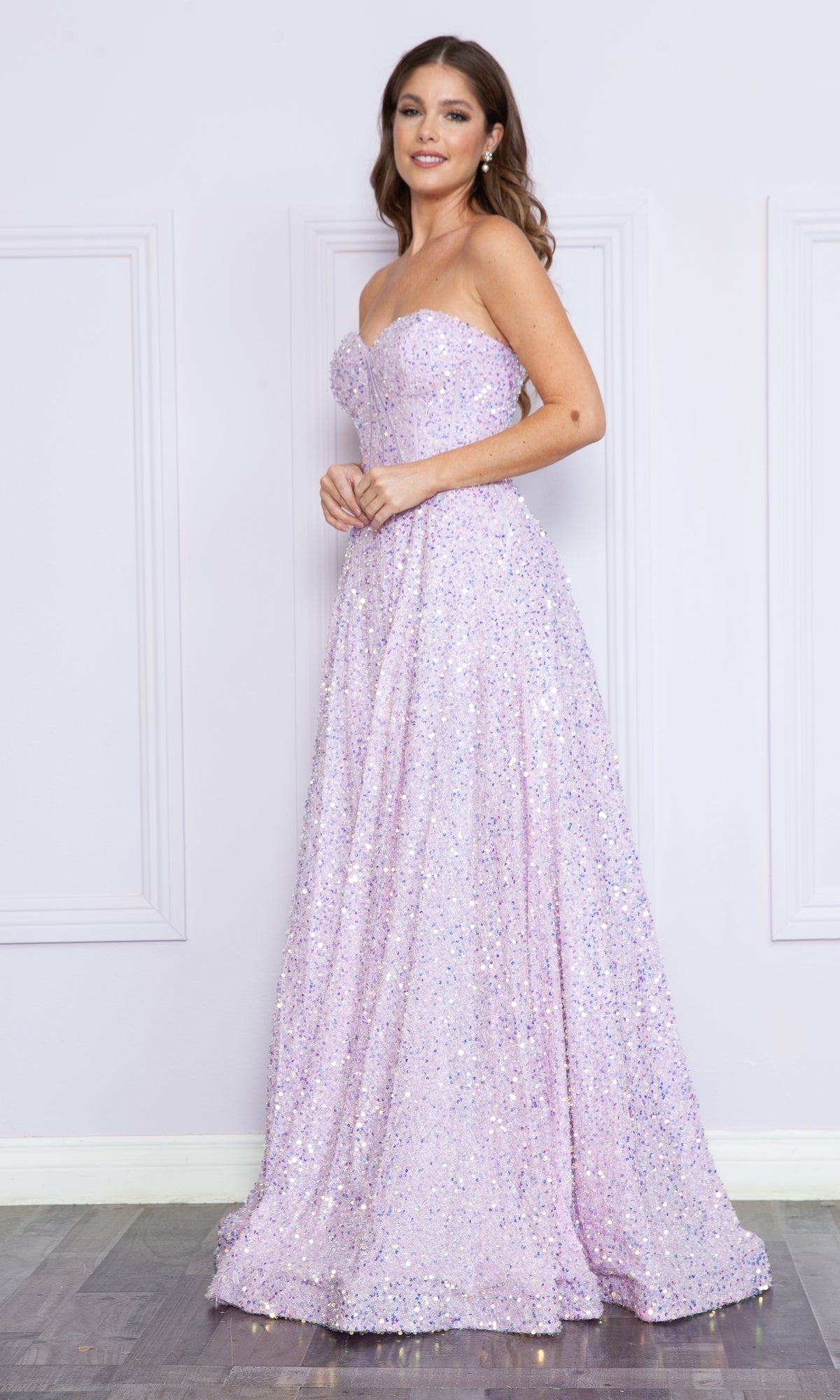 A woman models the Poly USA 9152 Strapless Sequin Prom Ball Gown, a floor-length light purple dress, standing against a light-colored wall with decorative molding.