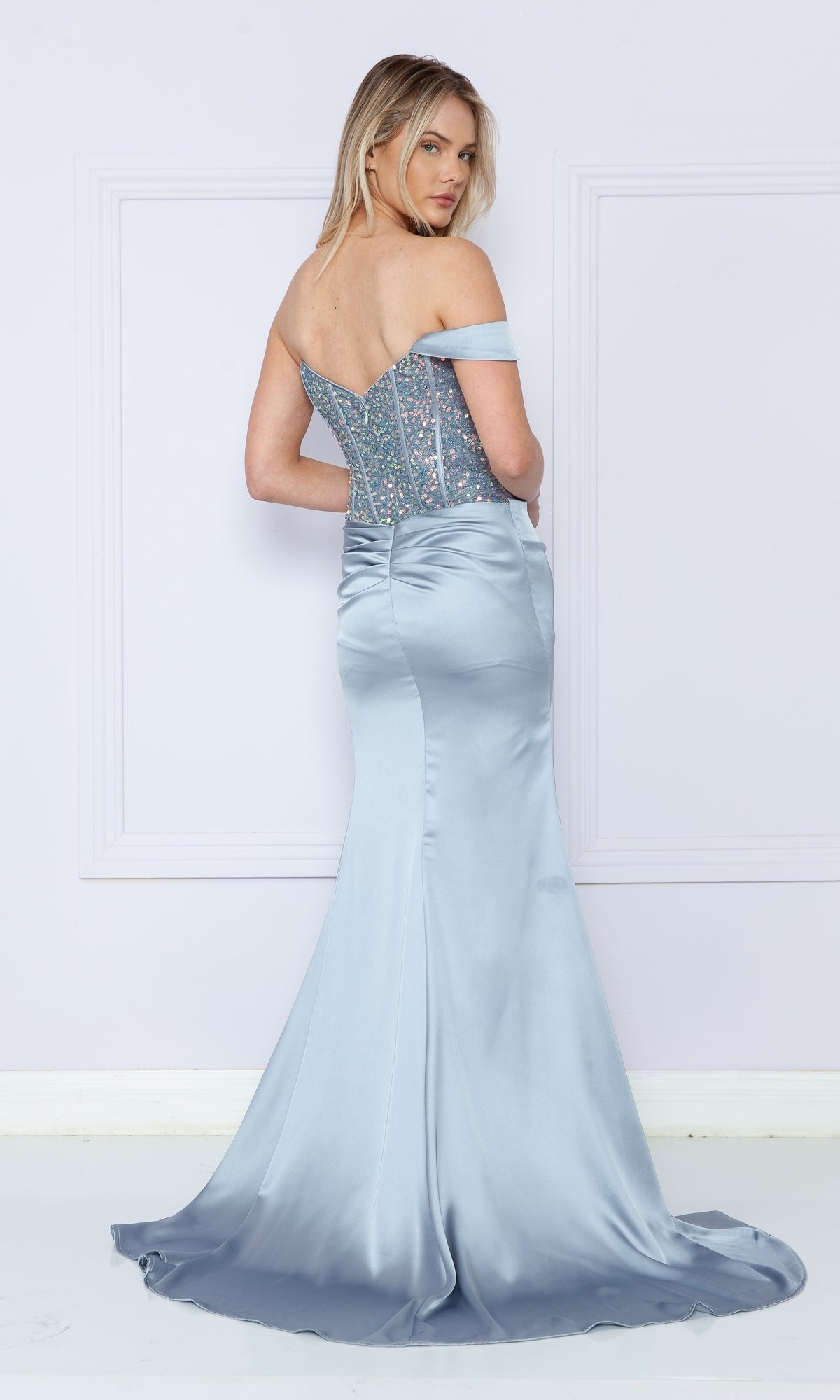 A woman in the One-Shoulder Sequin-Bodice Long Prom Dress 9178 stands facing away, showcasing the elegant back details and satin train of the silver-blue gown.