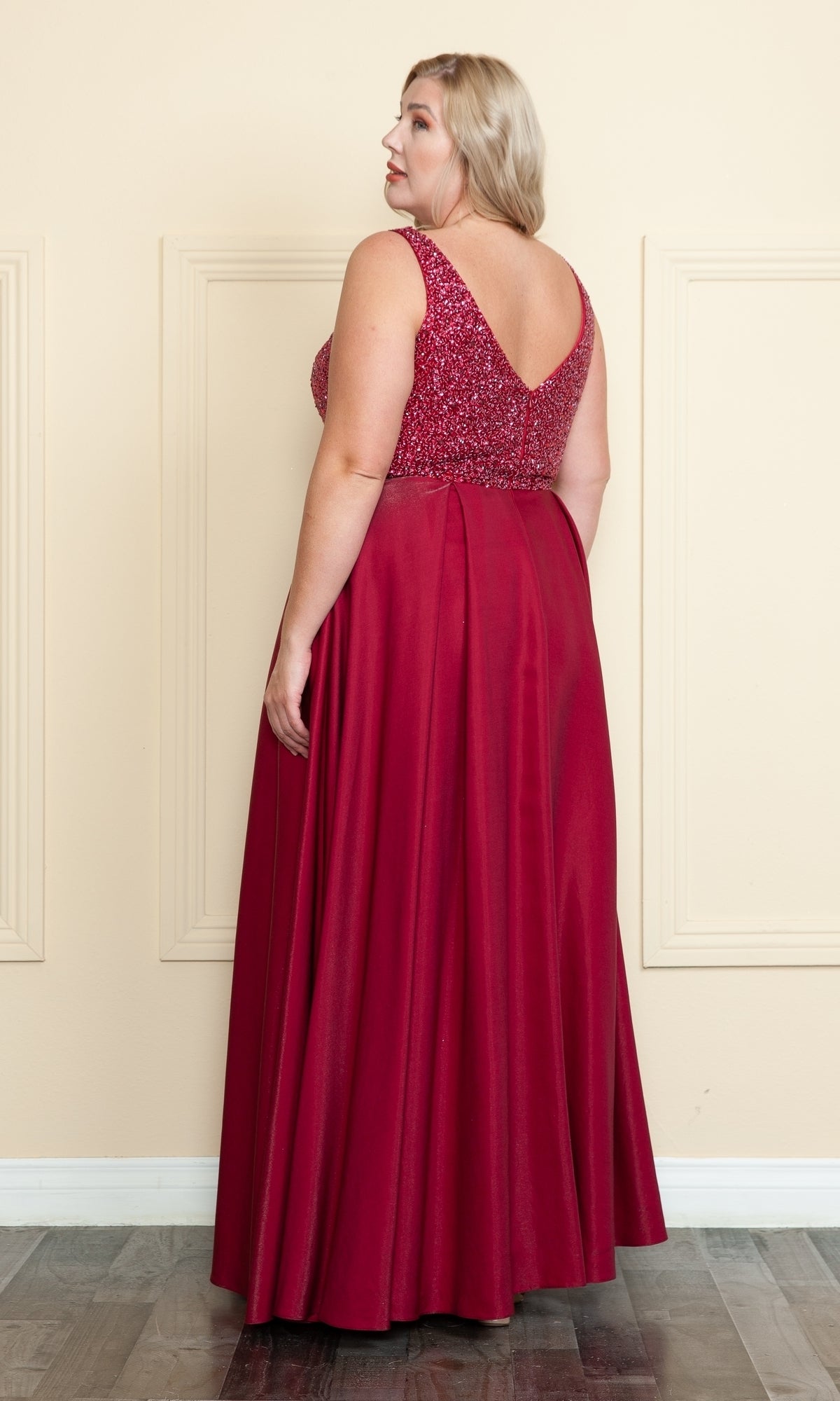 A woman models the Beaded-Bodice Plus-Size Long Prom Dress W1066, a sleeveless red gown with a beaded bodice and V-shaped back, standing to showcase its elegant floor-length design.