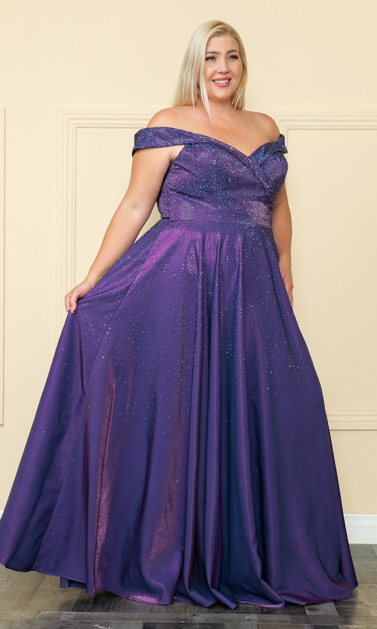 A woman in the Plus-Size Long Beaded Prom Dress with Pockets W1112, featuring an off-the-shoulder neckline and sparkly details, stands indoors against a beige wall.