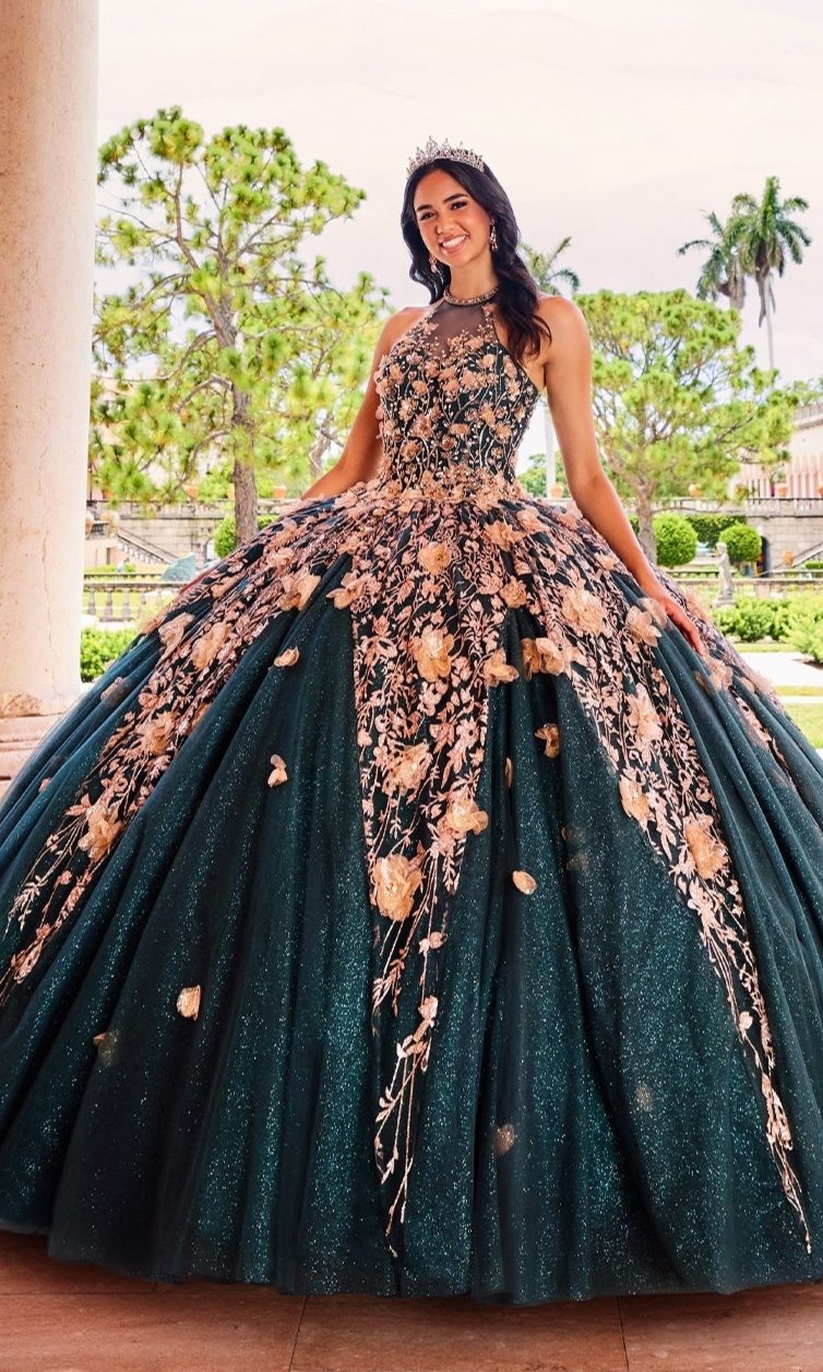 A young woman poses outdoors by a stone column, wearing the High-Neck Princesa Quinceañera Dress PR12262 in dark green with gold embroidery and a tiara, with trees in the background.