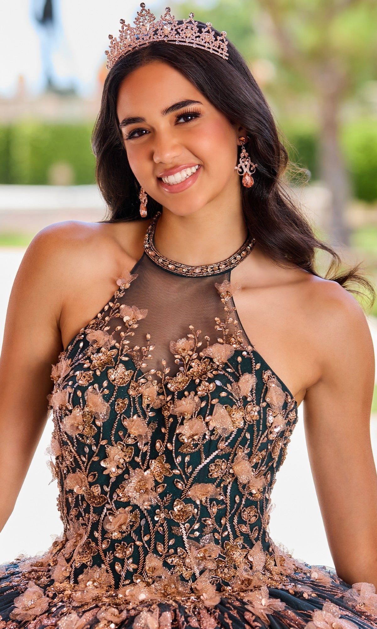 A young woman wearing a jeweled tiara and the High-Neck Princesa Quinceañera Dress PR12262, adorned with ornate floral beading, smiles at the camera.