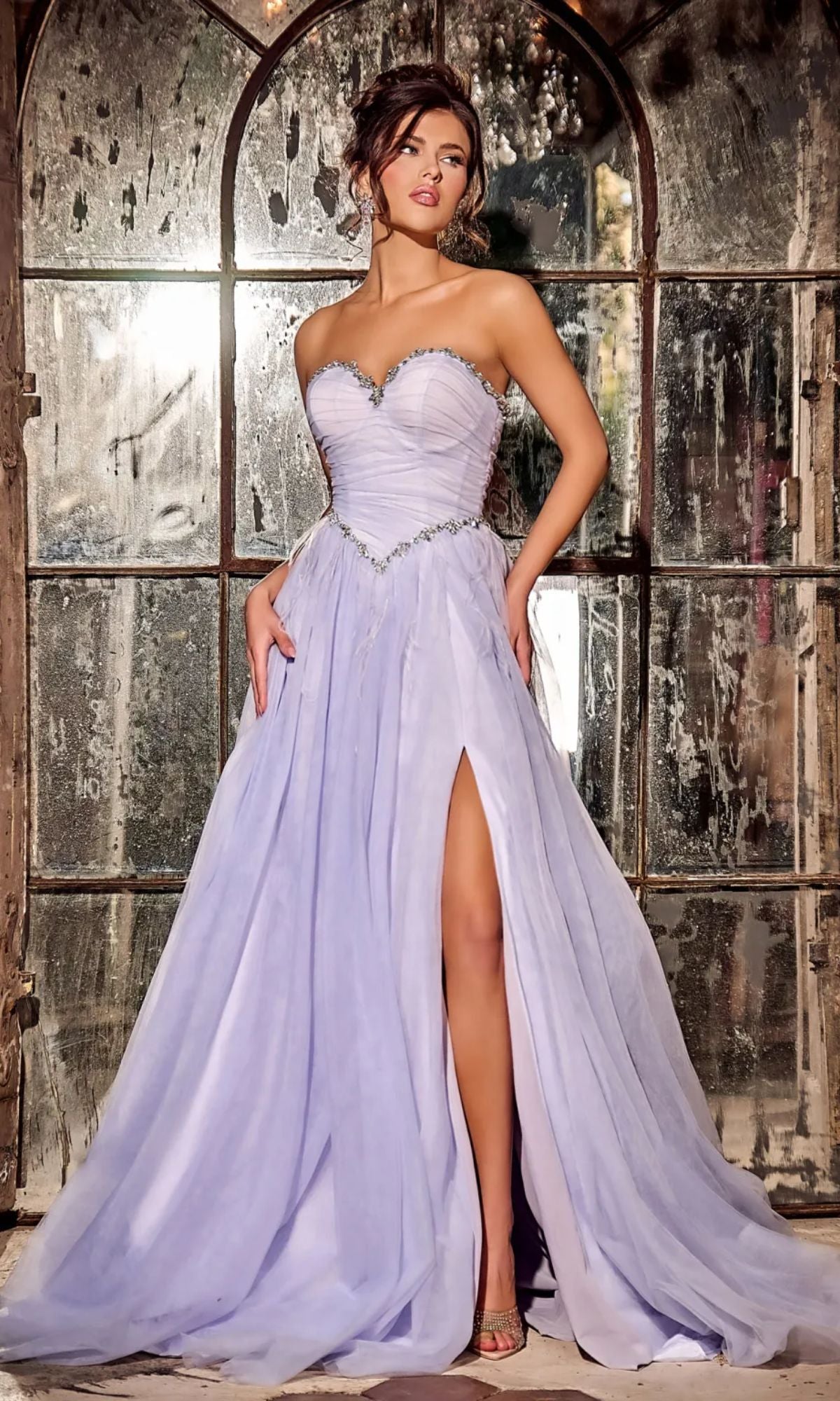 A woman in the Long Prom Dress PS24632 by Portia and Scarlett—an A-line tulle gown with strapless, beaded sweetheart neckline, and jeweled trim—stands before an old arched window, embodying timeless elegance.