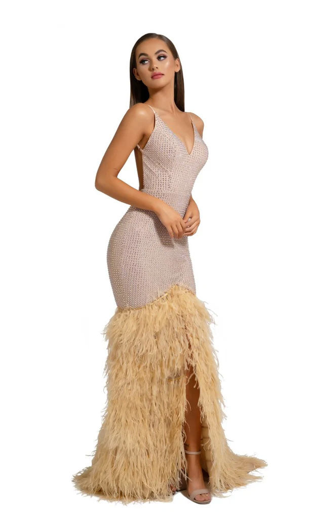 A woman wears the Portia and Scarlett Long Formal Dress PS6826, a form-fitting beige gown featuring a V-neckline and feather trim on the lower half, standing against a white background.