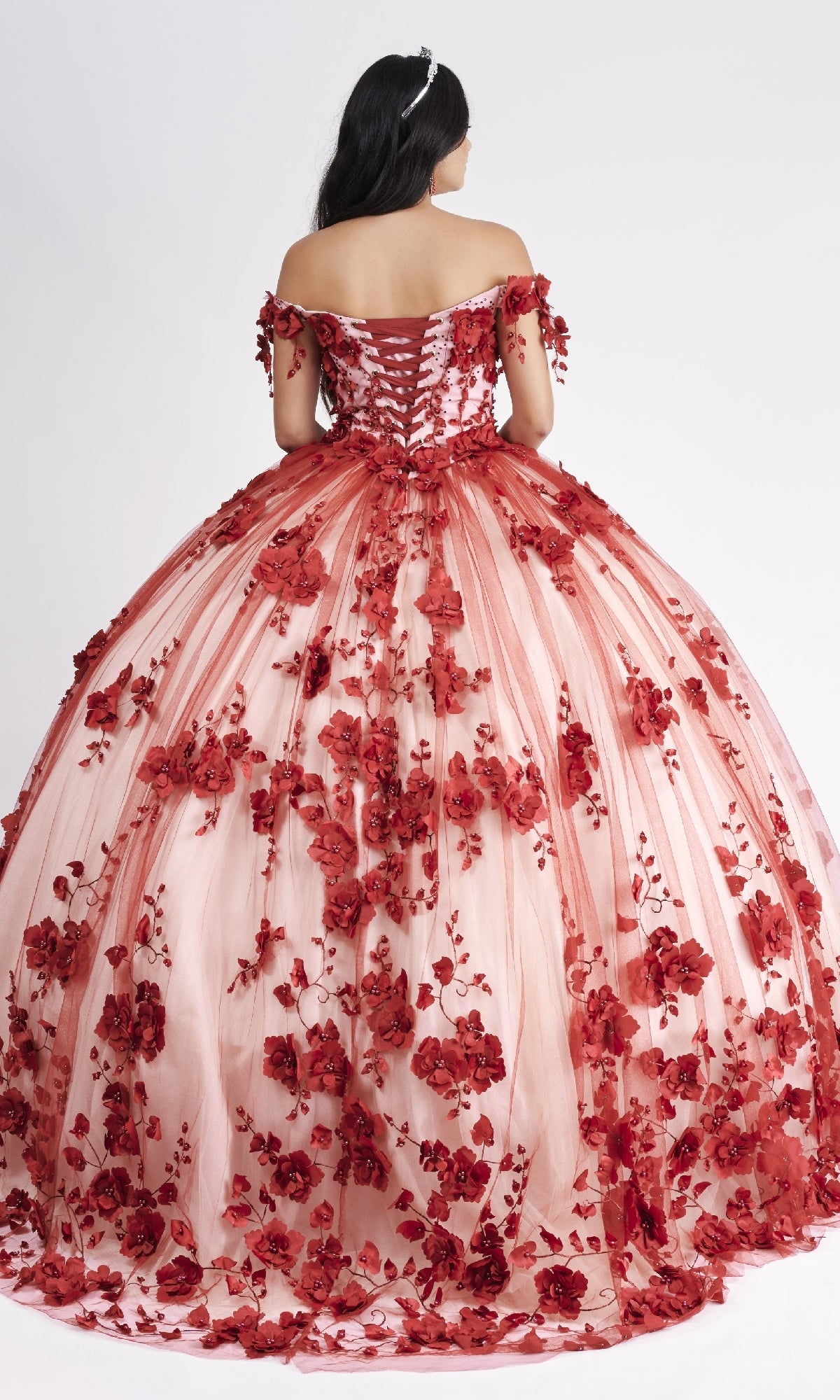 Woman in the Nina Canacci Q102 Long Quinceanera Dress—red and pink off-the-shoulder ball gown with 3D floral appliques—shown from the back against a plain white background.