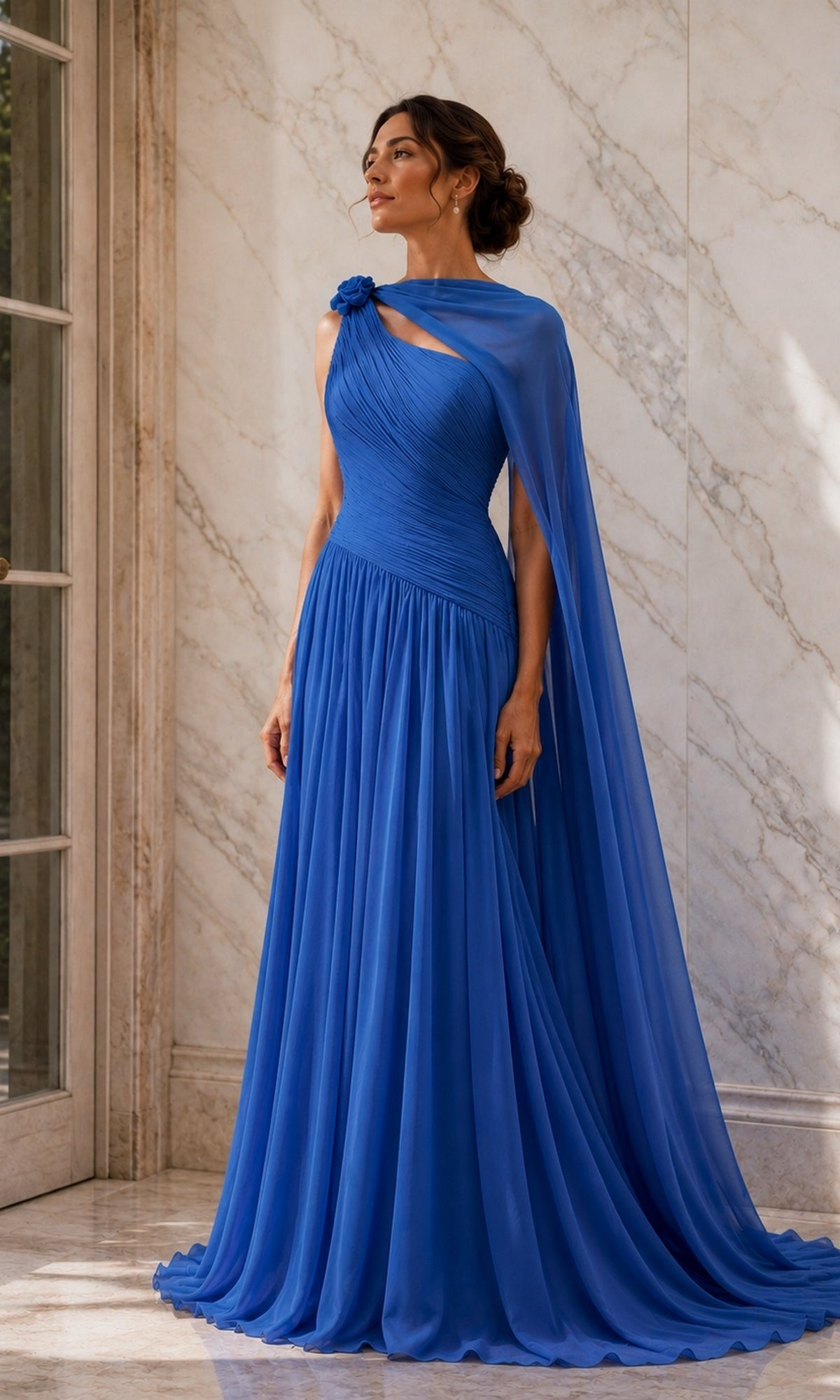 A woman in a Rina Di Montella R110 one shoulder cape long formal dress in ocean blue, featuring a one-shoulder chiffon design, pleated bodice, floor-length hem, and an attached sheer cape.