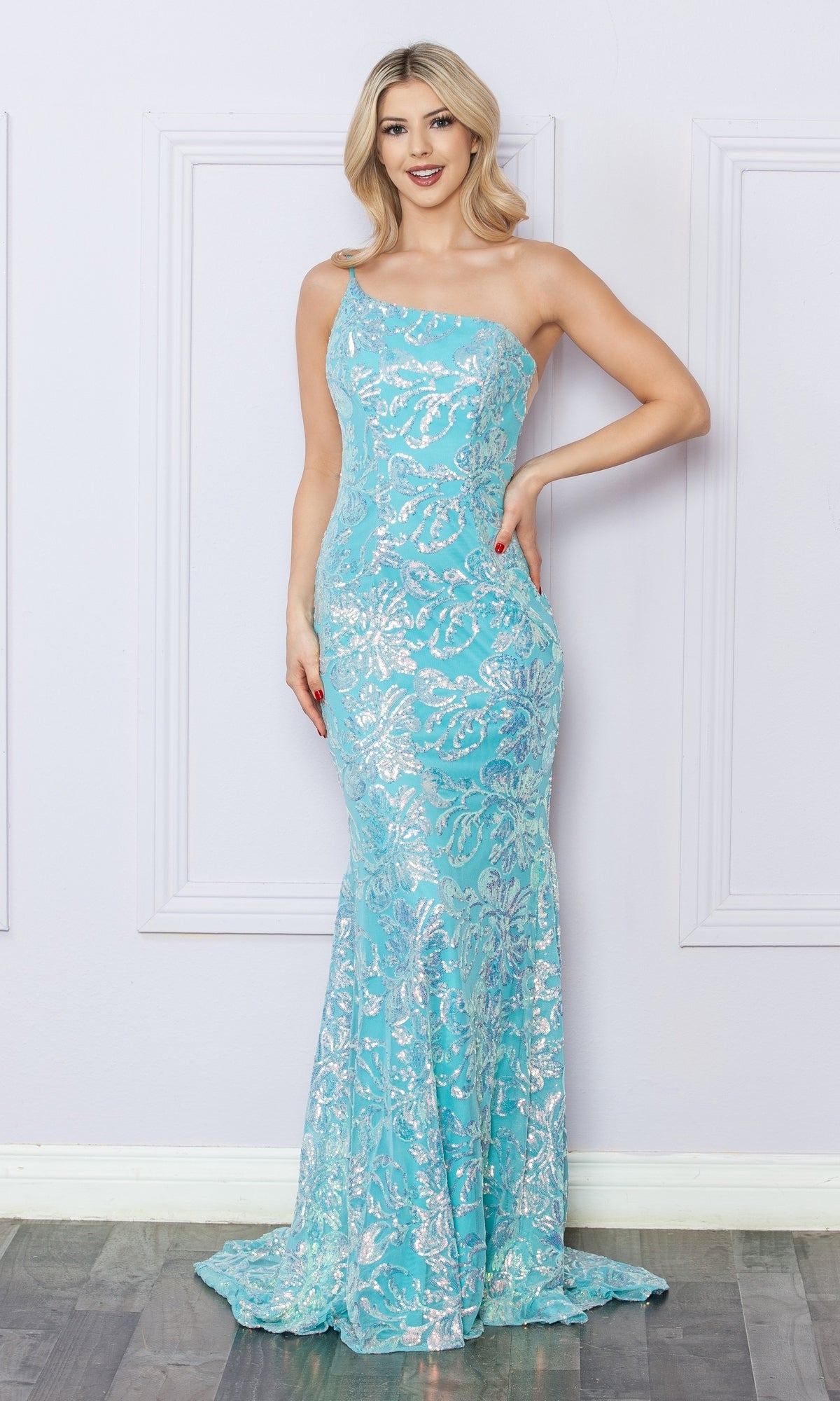 A woman stands by a light-colored wall wearing the One-Shoulder Long Sequin-Print Prom Dress R1308, featuring silver sequin patterns on a light blue, floor-length gown.