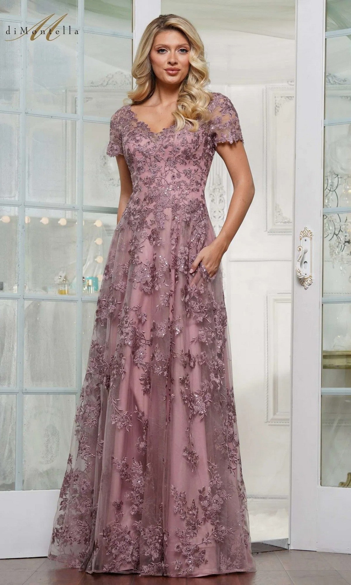 A woman poses indoors in front of glass-paneled doors wearing the Rina Di Montella RD3248, a dusty rose long formal dress featuring an a-line skirt and beaded floral embroidery.