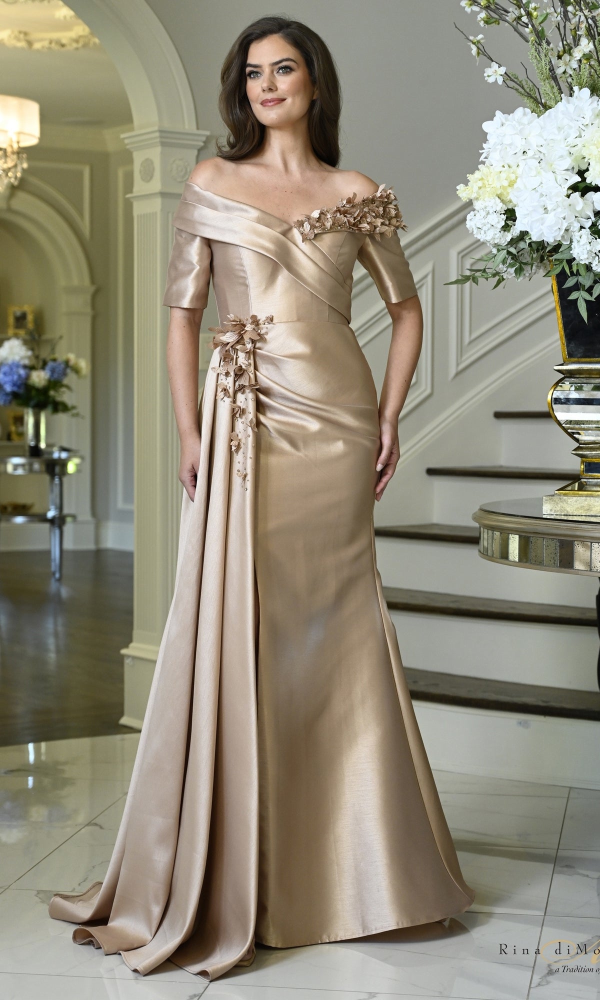 Rose gold off-the-shoulder mermaid formal dress, Rina Di Montella RD3611, featuring floral embellishments along the neckline and hip.