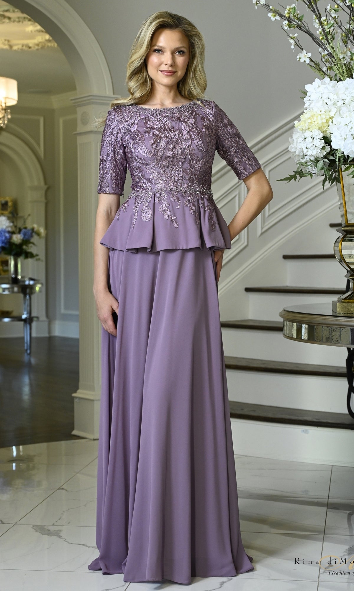 A woman wearing a Victorian Lilac Beaded Lace Peplum Long Formal Dress: Rina Di Montella RD3642, featuring a refined bodice, elbow-length sleeves, and a peplum waist.