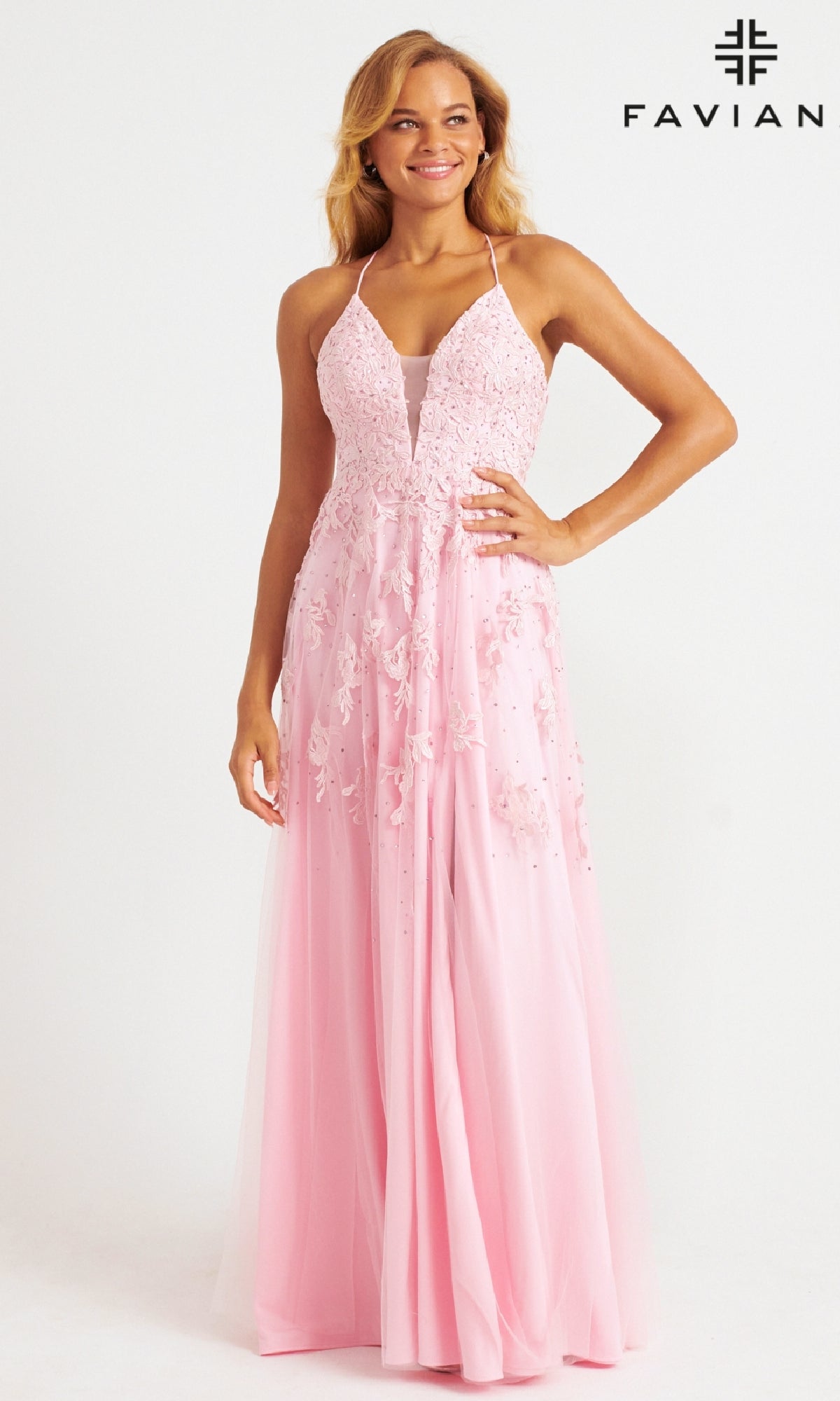 A woman smiles in a Faviana Embroidered A-Line Long Prom Dress—light pink, sleeveless, and adorned with lace and 3D floral embroidery—standing against a plain white background with the