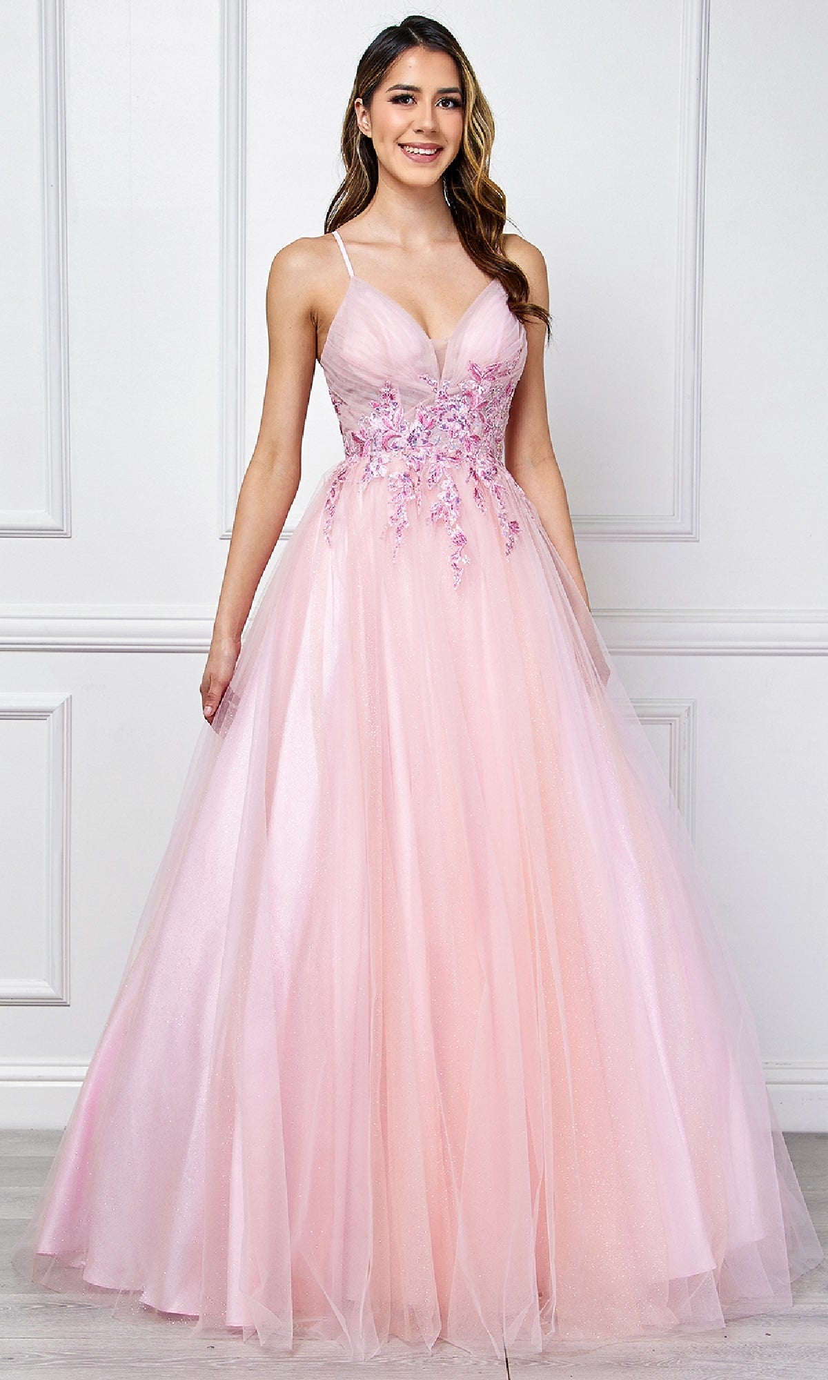 A woman stands indoors wearing the Amelia Couture SU088 long pastel prom ball gown, featuring thin straps, a floral embroidered bodice, and a full tulle skirt.