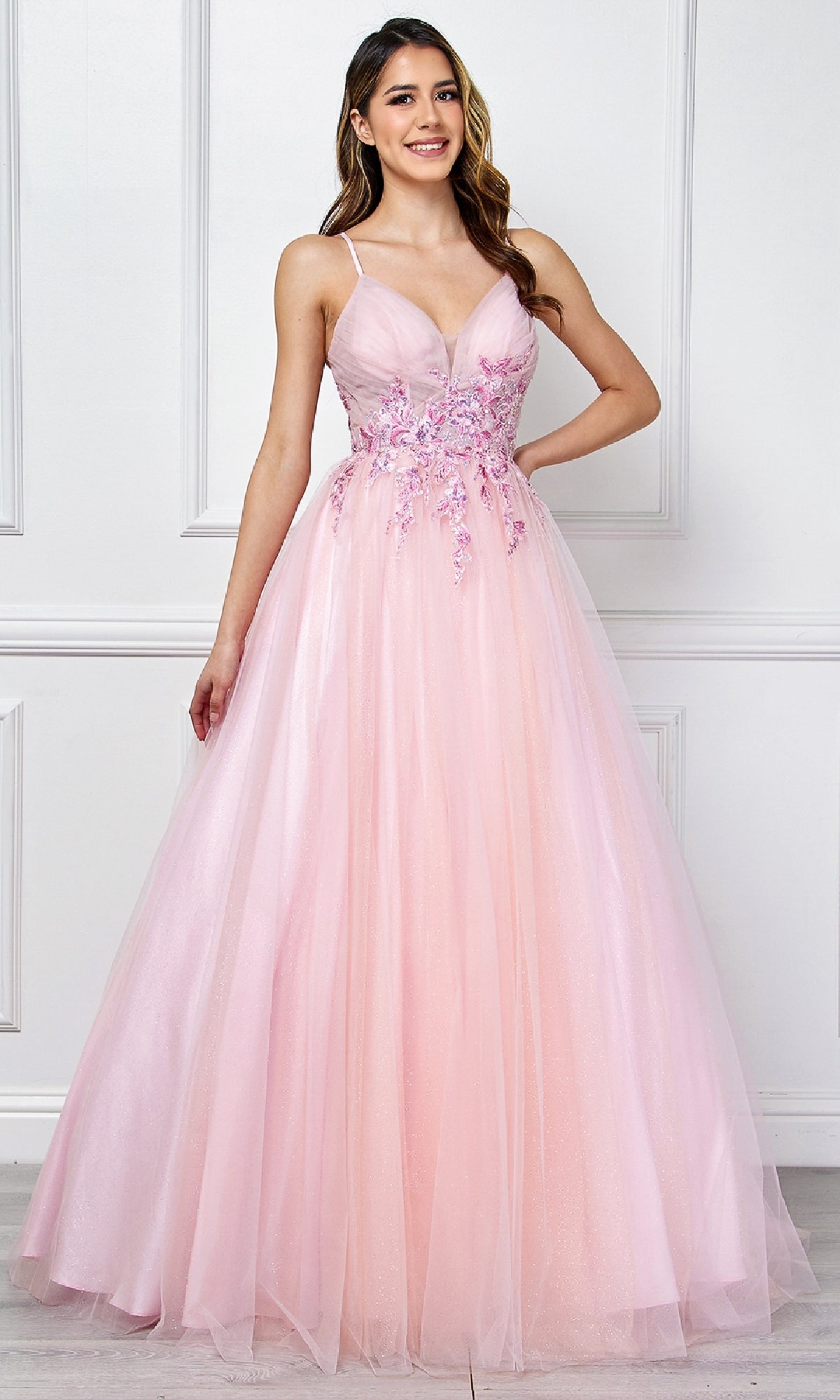 A woman stands wearing the Amelia Couture SU088, a long pastel prom ball gown with thin straps, floral embroidered bodice, and a tulle skirt.