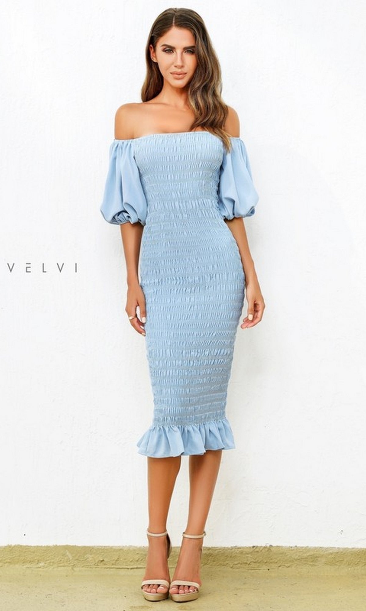 A woman models the Skyla Knee-Length Puff-Sleeve Wedding-Guest Dress in light blue, featuring an off-the-shoulder smocked bodice, puff sleeves, and a ruffled hem, shown against a plain white background.