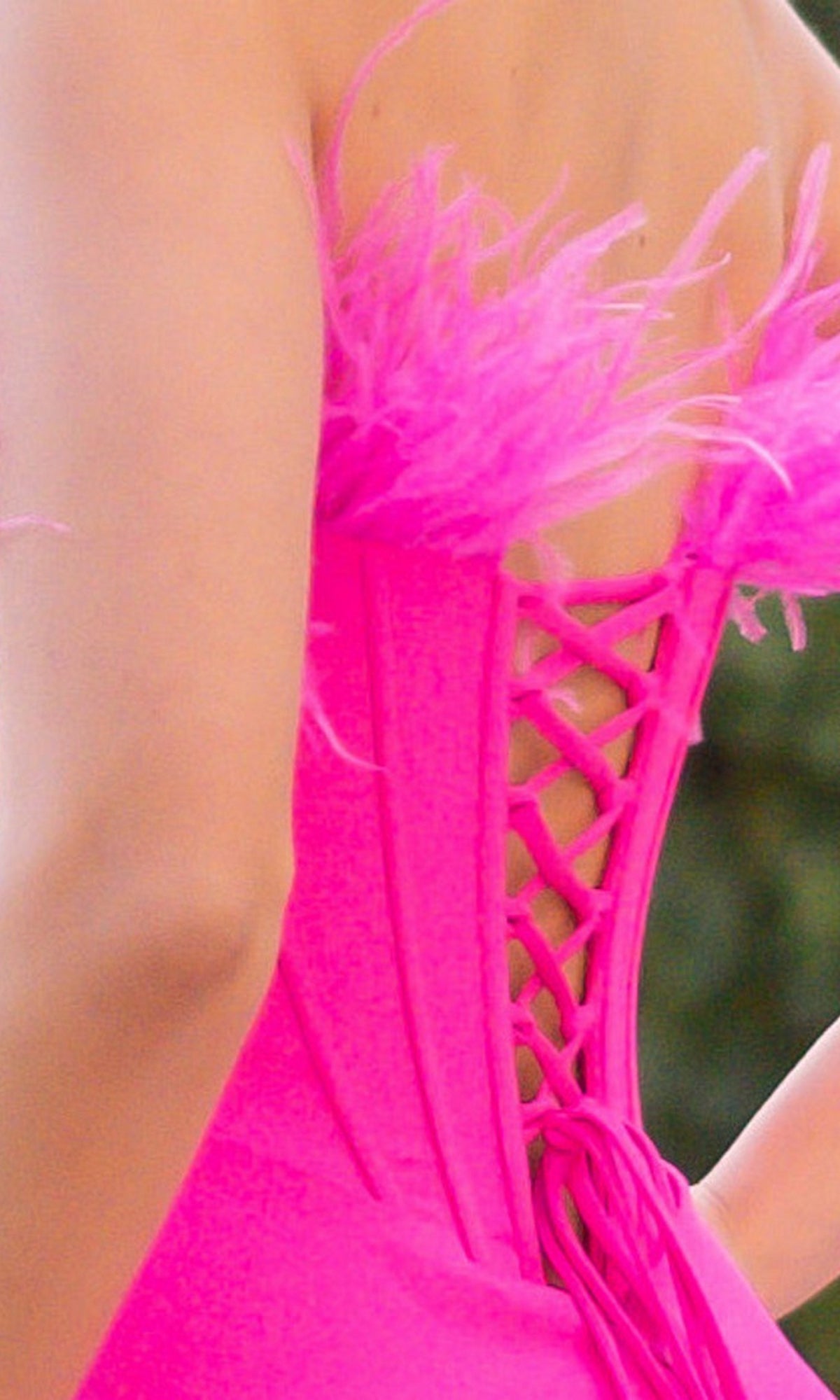 Close-up of a person wearing the Velvi Feathered Strapless Long Prom Dress Sloane—a bright pink, lace-up gown with feather trim and a corset-style back, perfect for any formal event.