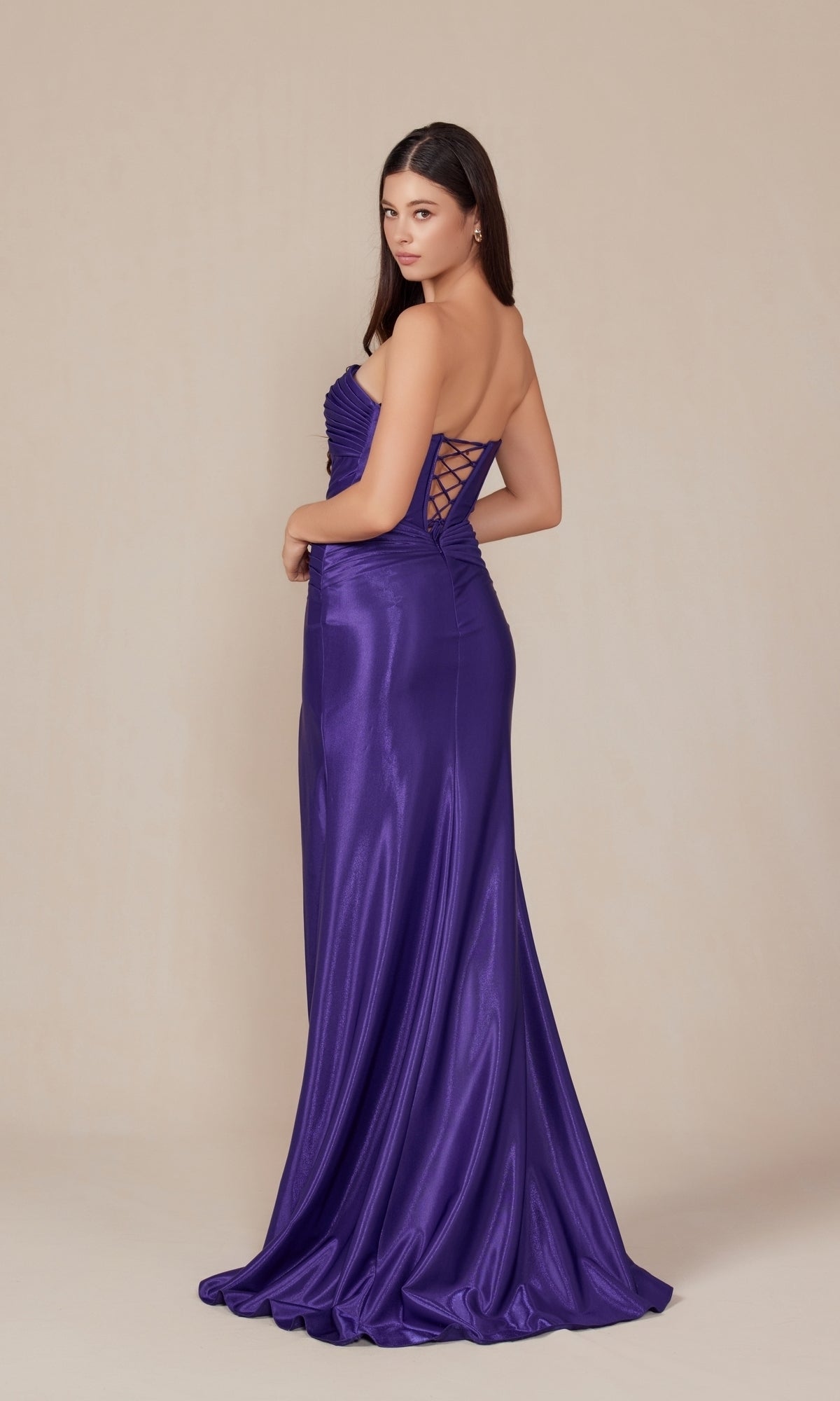 A woman poses against a plain beige background in the Strapless Lace-Up Long Prom Gown: Nox Anabel T1489—an elegant, shiny purple formal dress with a lace-up back detail.