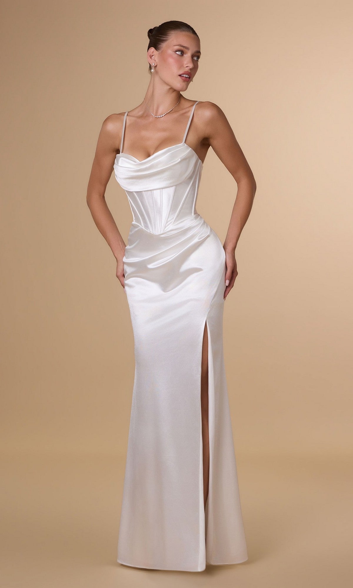 A woman in the off-white Amoris T815W long prom dress, featuring a satin corset bodice and a thigh-high slit, stands against a beige background.