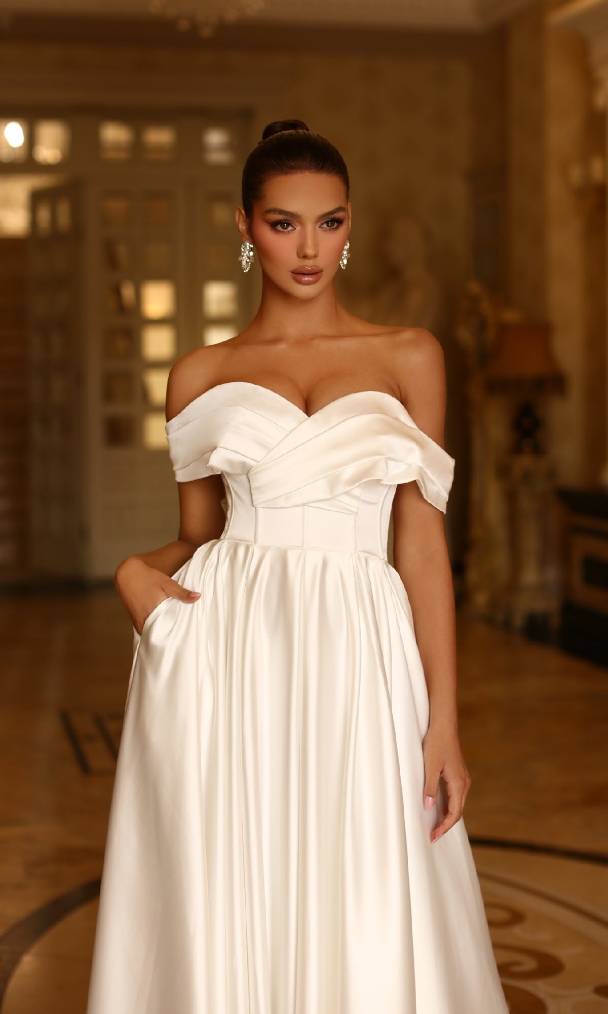 A woman stands indoors, hand in pocket, wearing the Off-White Long Prom Ball Gown Tina Holly TE207W and looking directly at the camera.