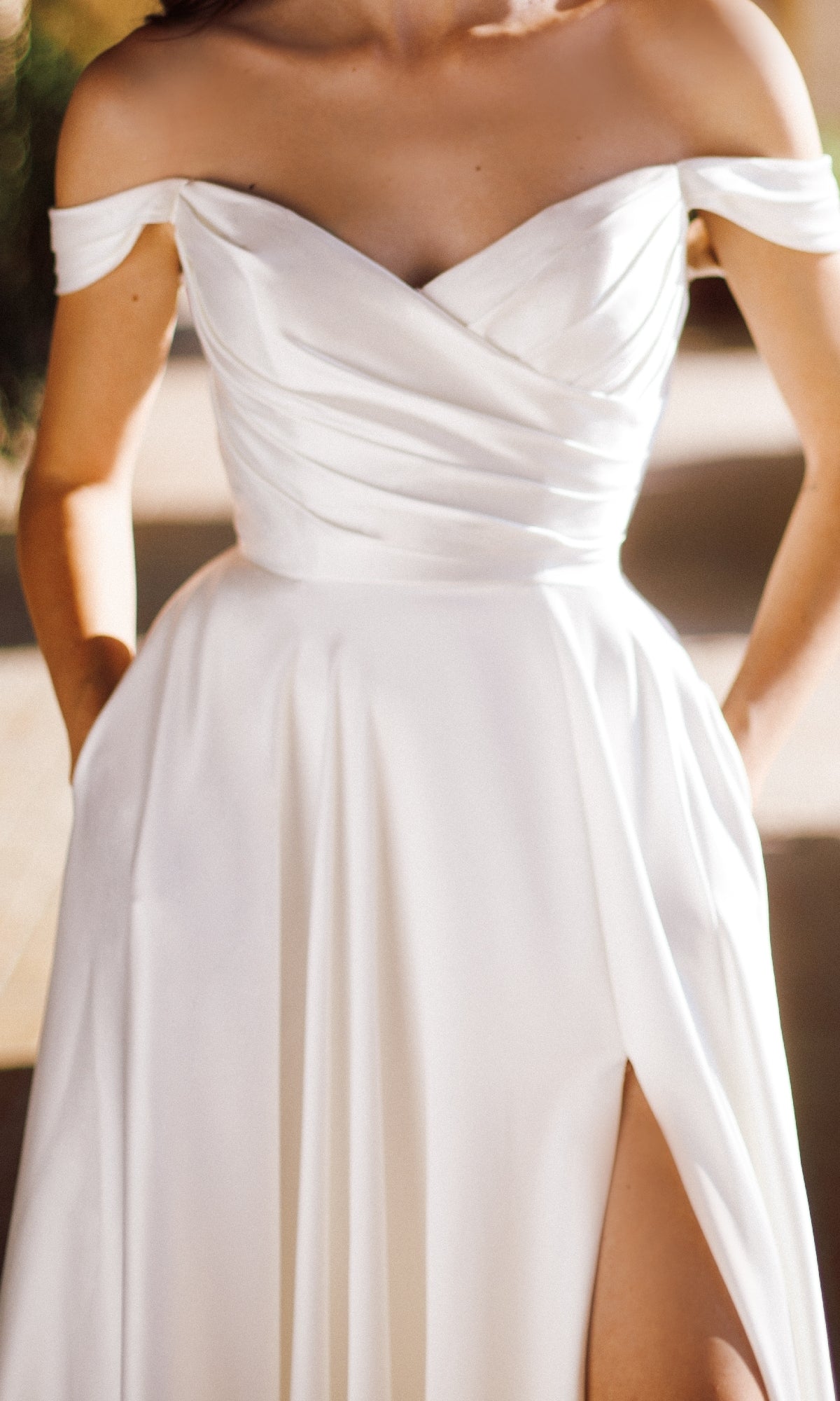 A woman wearing the Long Formal Dress: Tina Holly TE565—an off-the-shoulder, a-line wedding dress with a pleated bodice, thigh-high slit, and pockets—perfect for modern brides seeking elegance.