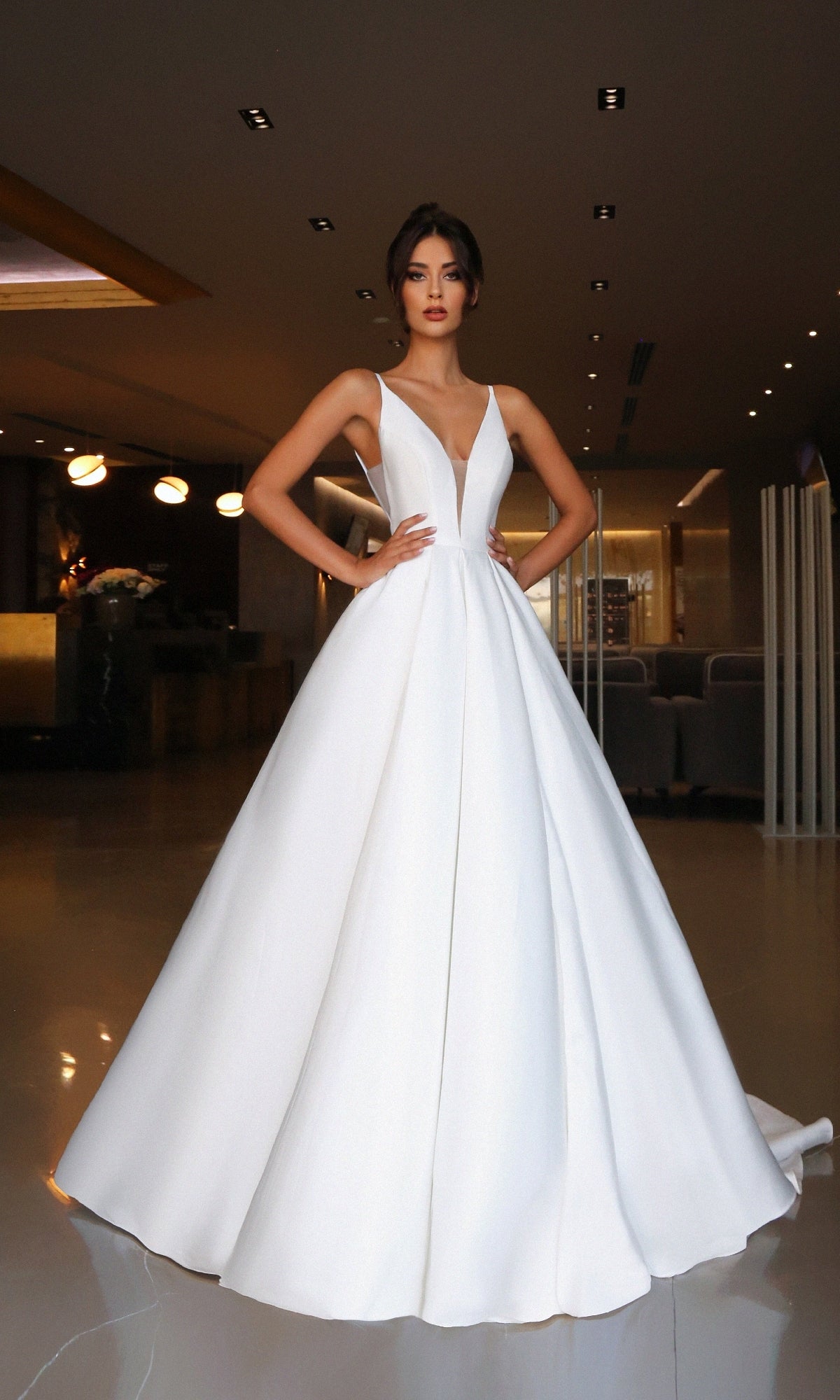 A woman in the Off-White Mikado Prom Ball Gown: Tina Holly TF002 stands in a modern, softly-lit interior with her hands on her hips.