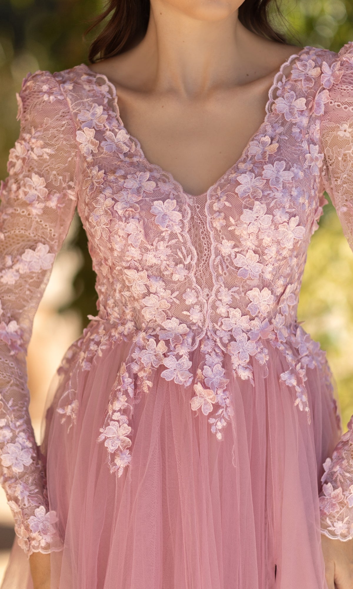 A woman photographed from shoulders to mid-waist wears the Long Pink Formal Dress: Tina Holly TF318F, featuring a pastel hue, lace bodice, floral embroidery, and long sheer sleeves.