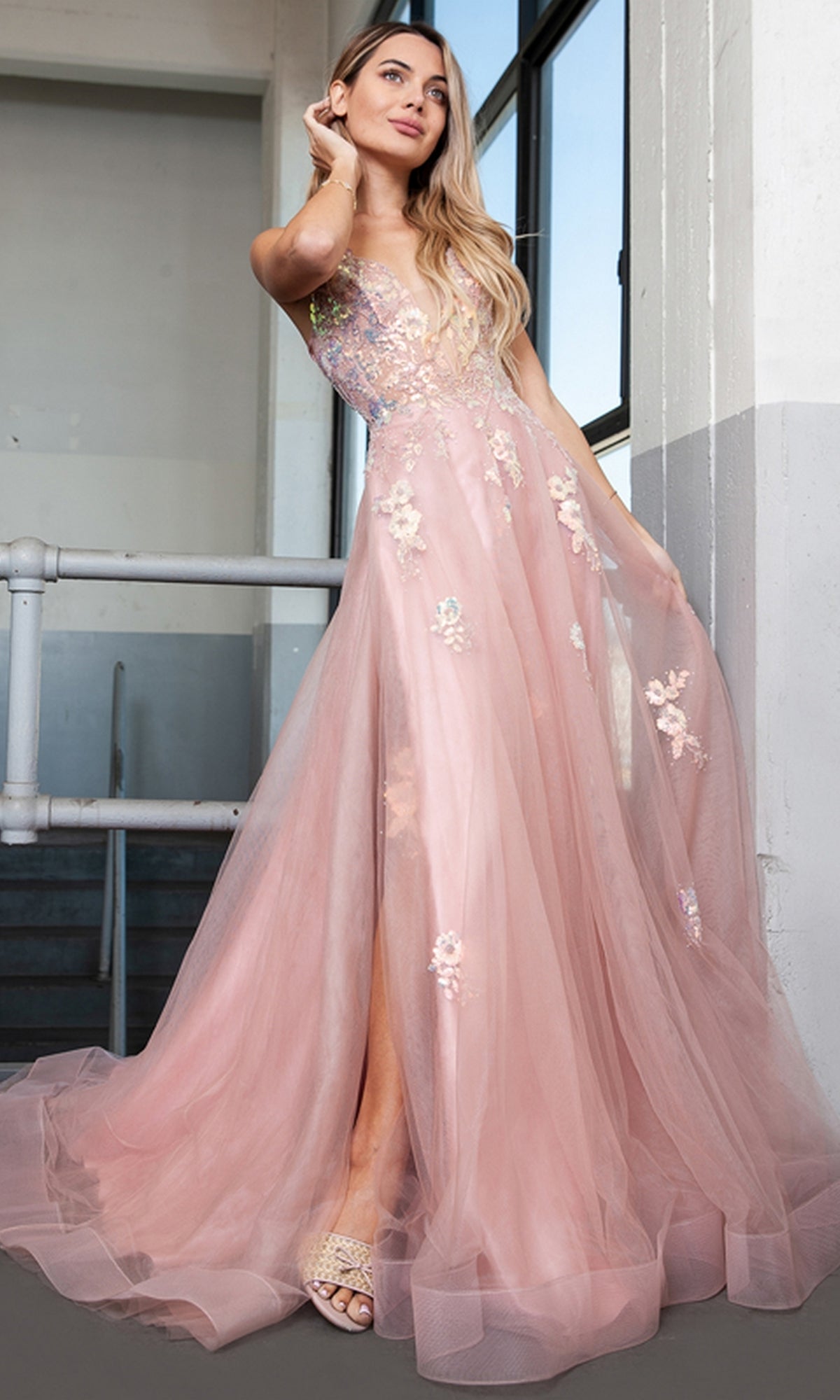A woman stands indoors wearing the Floral-Embellished Pastel Prom Ball Gown TM1003, a sleeveless, floor-length dress with floral details and a flowing tulle skirt.