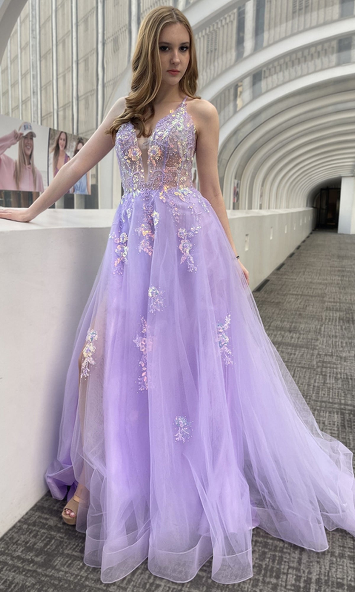 A young woman stands indoors wearing the Floral-Embellished Pastel Prom Ball Gown TM1003, featuring floral accents and a sheer tulle skirt.