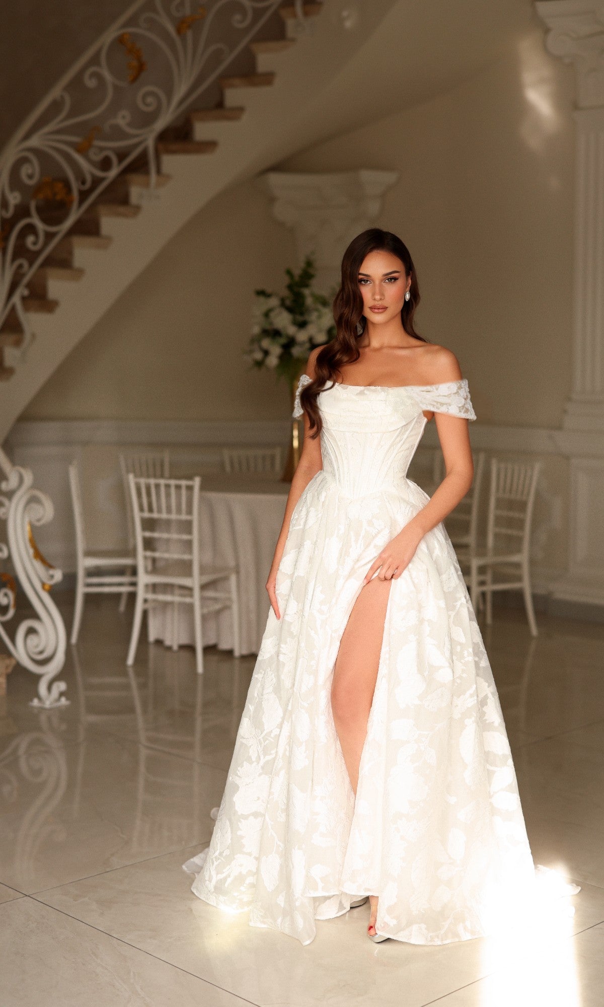 Woman wearing a Tina Holly TW623 long wedding dress featuring an off-the-shoulder floral design and a high leg slit.