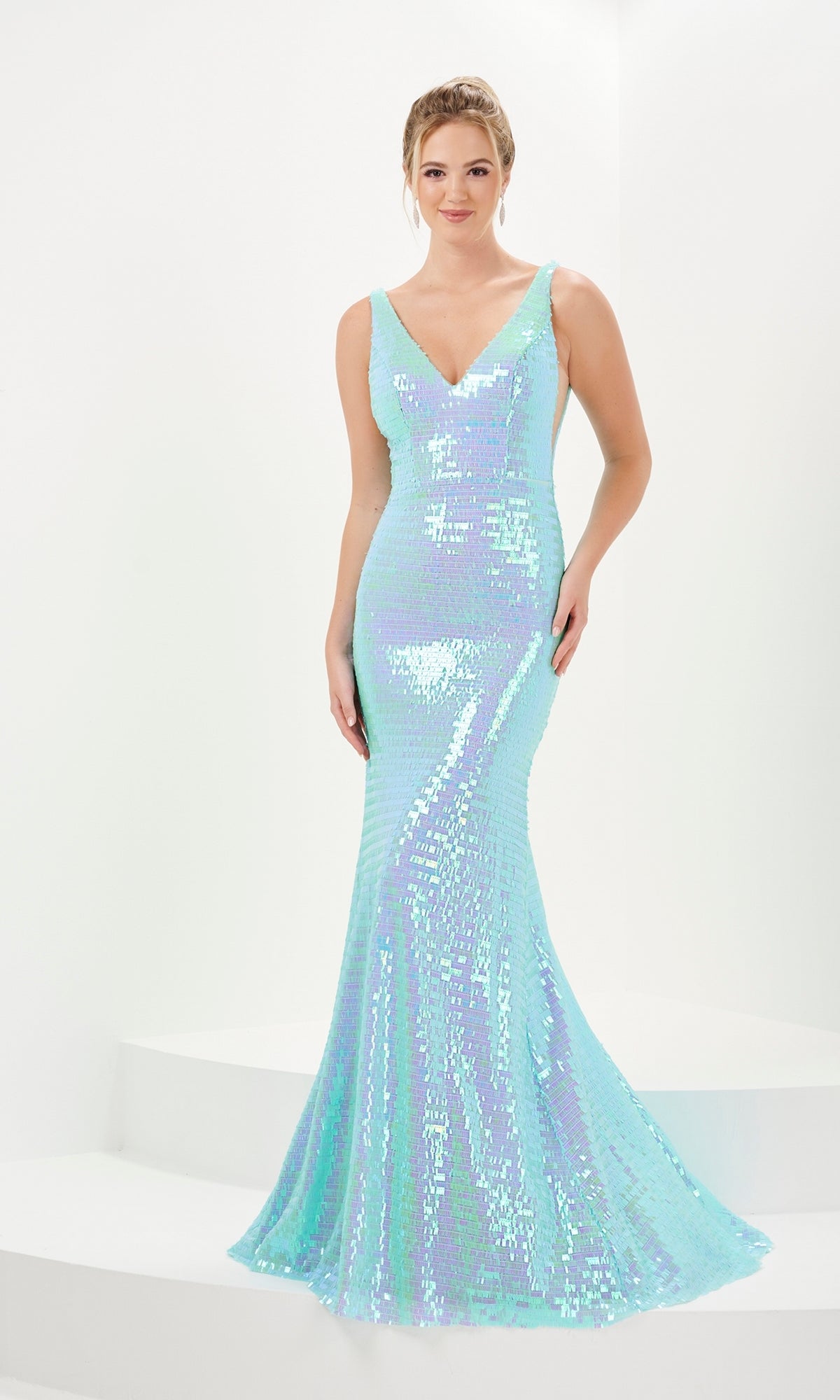 A woman wears the Micro-Fringe Long Prom Dress: Tiffany 16065, a fitted, sleeveless aqua evening gown with an iridescent finish and v-neckline, standing against a white background.