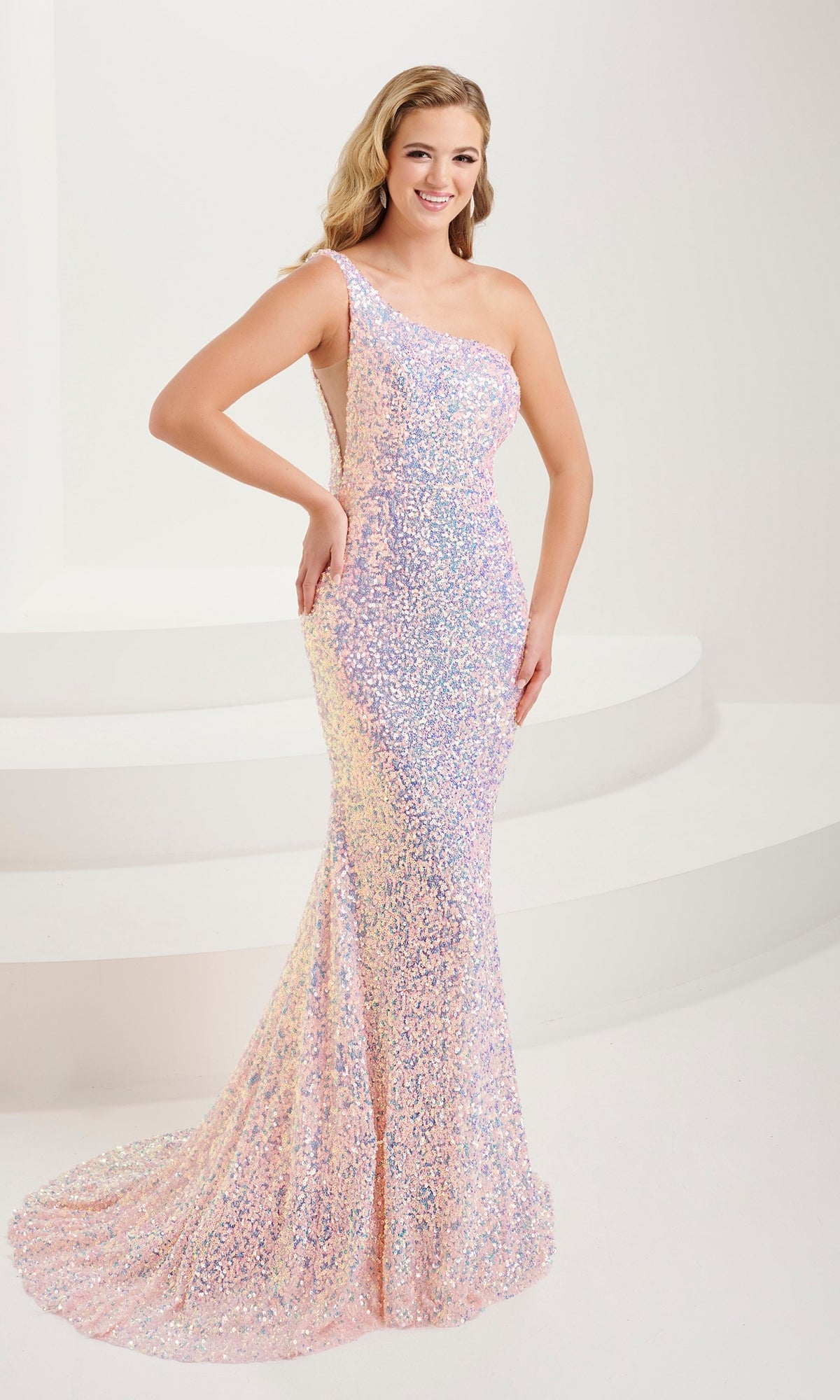 A woman stands on a white curved staircase wearing the Tiffany One-Shoulder Long Sequin Prom Dress 16114, a fitted iridescent gown with a dramatic train.