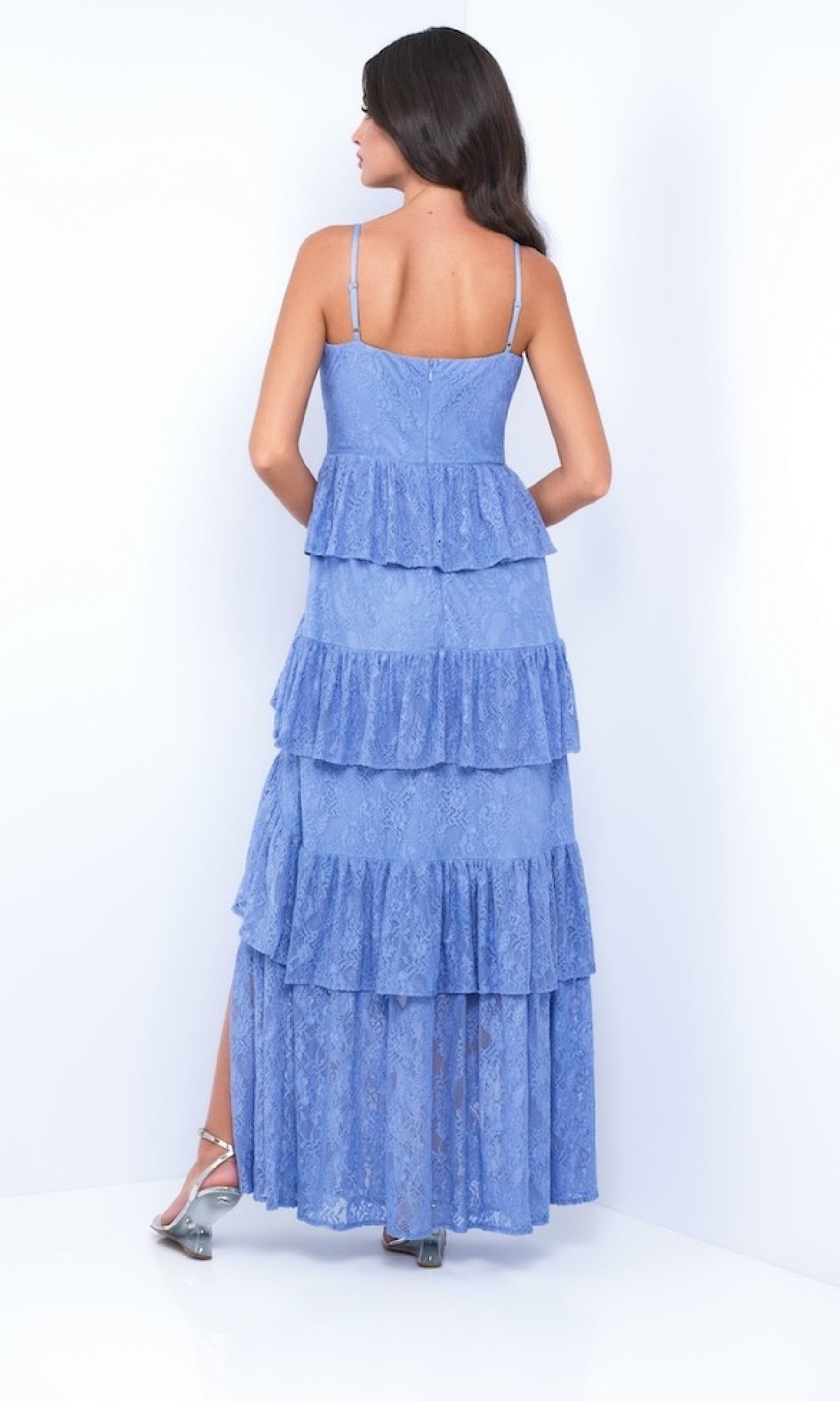 A woman stands with her back to the camera in a light blue Vanna by Velvi Ruffled Tiered Long Lace Prom Dress and metallic heeled sandals, set against a plain white background.